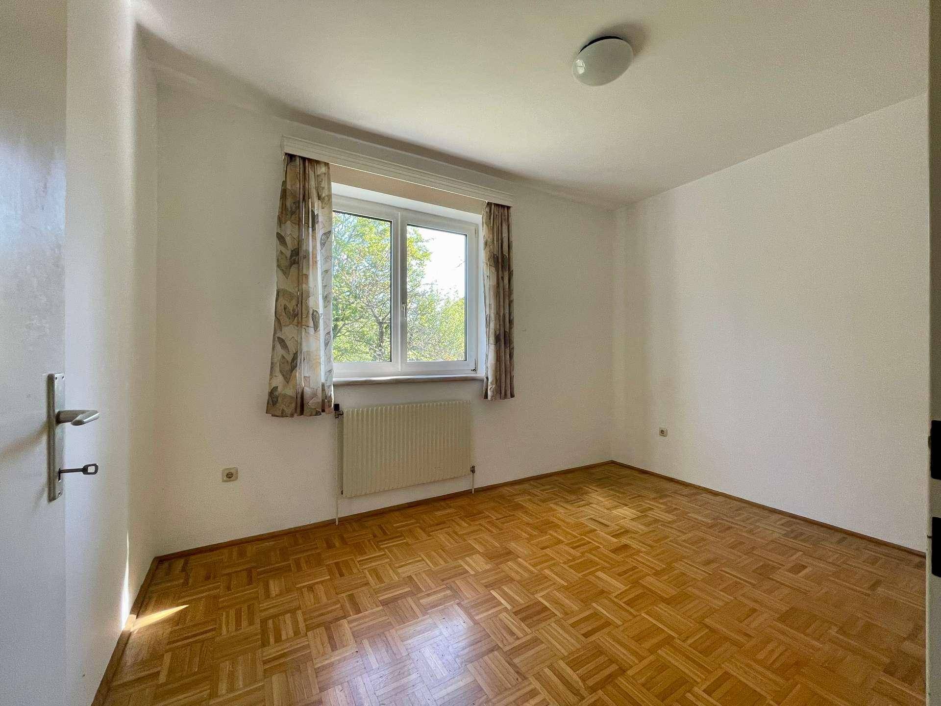 Weiteres helles Schlafzimmer mit Parkettboden und Blick ins Grüne.