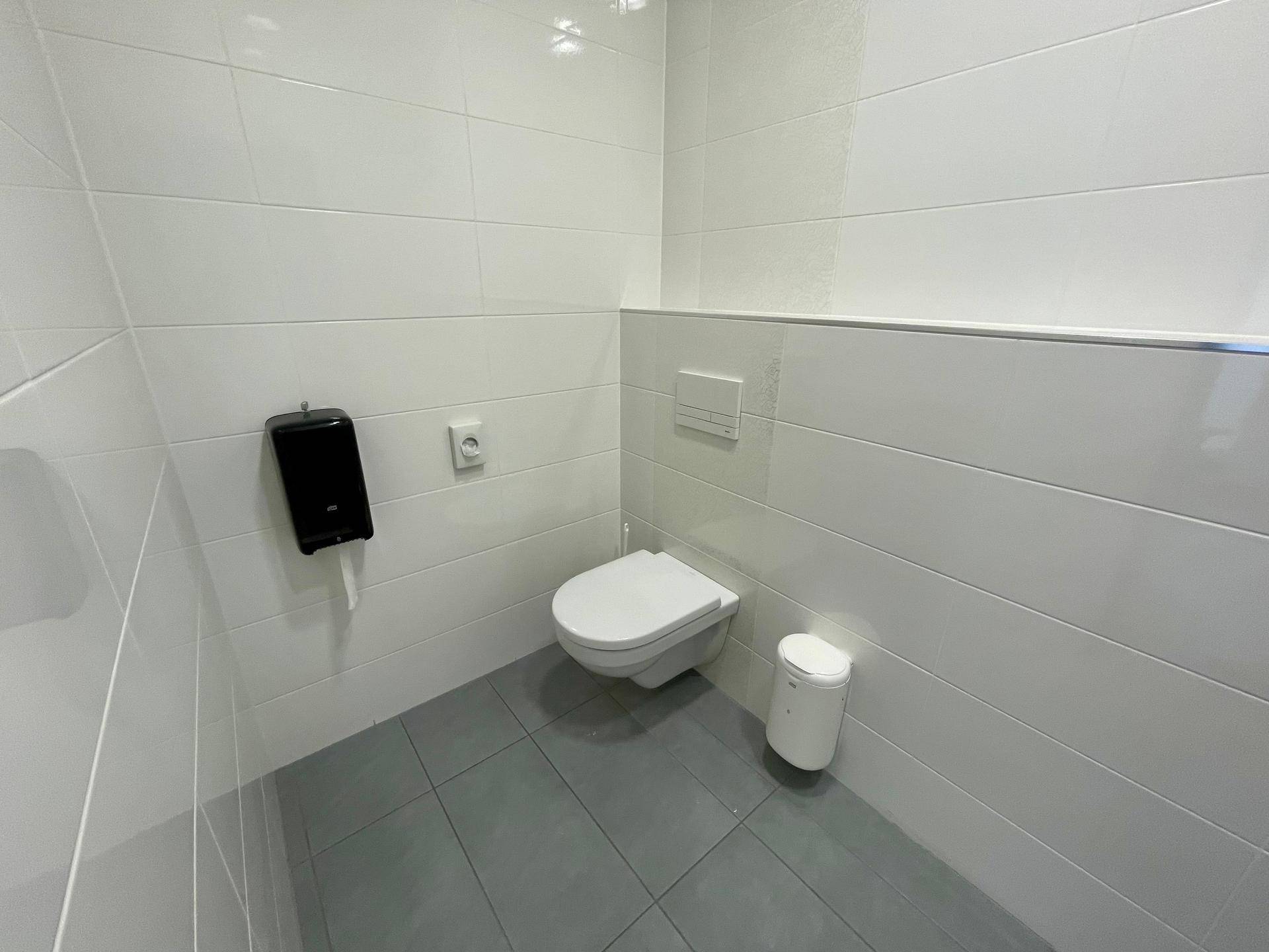Sauberer Toilettenraum mit weißen Fliesen und einer wandhängenden Toilette, minimalistisch und hygienisch.