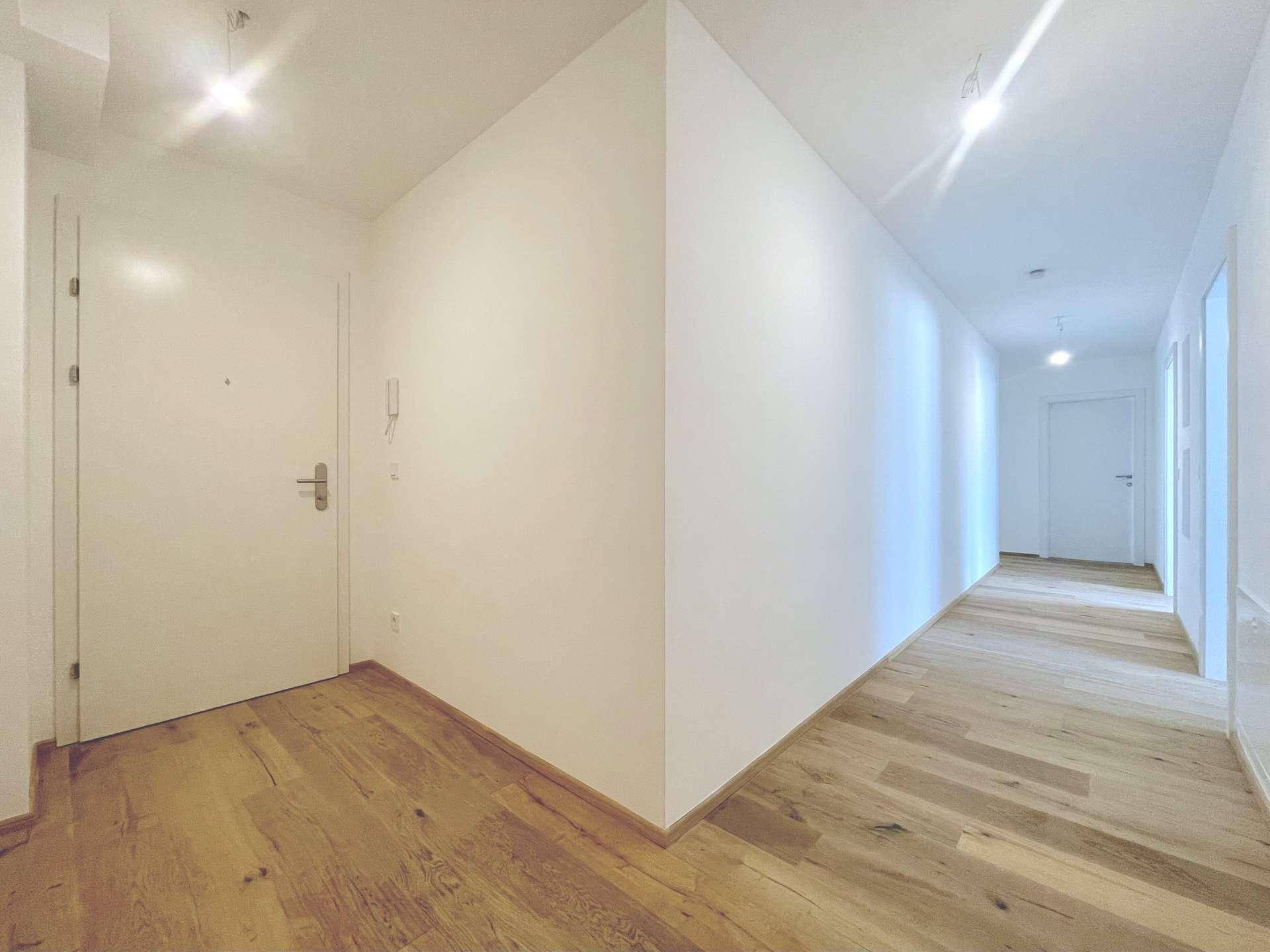 Heller Eingangsbereich und Flur mit elegantem Holzboden und weißen Wänden.