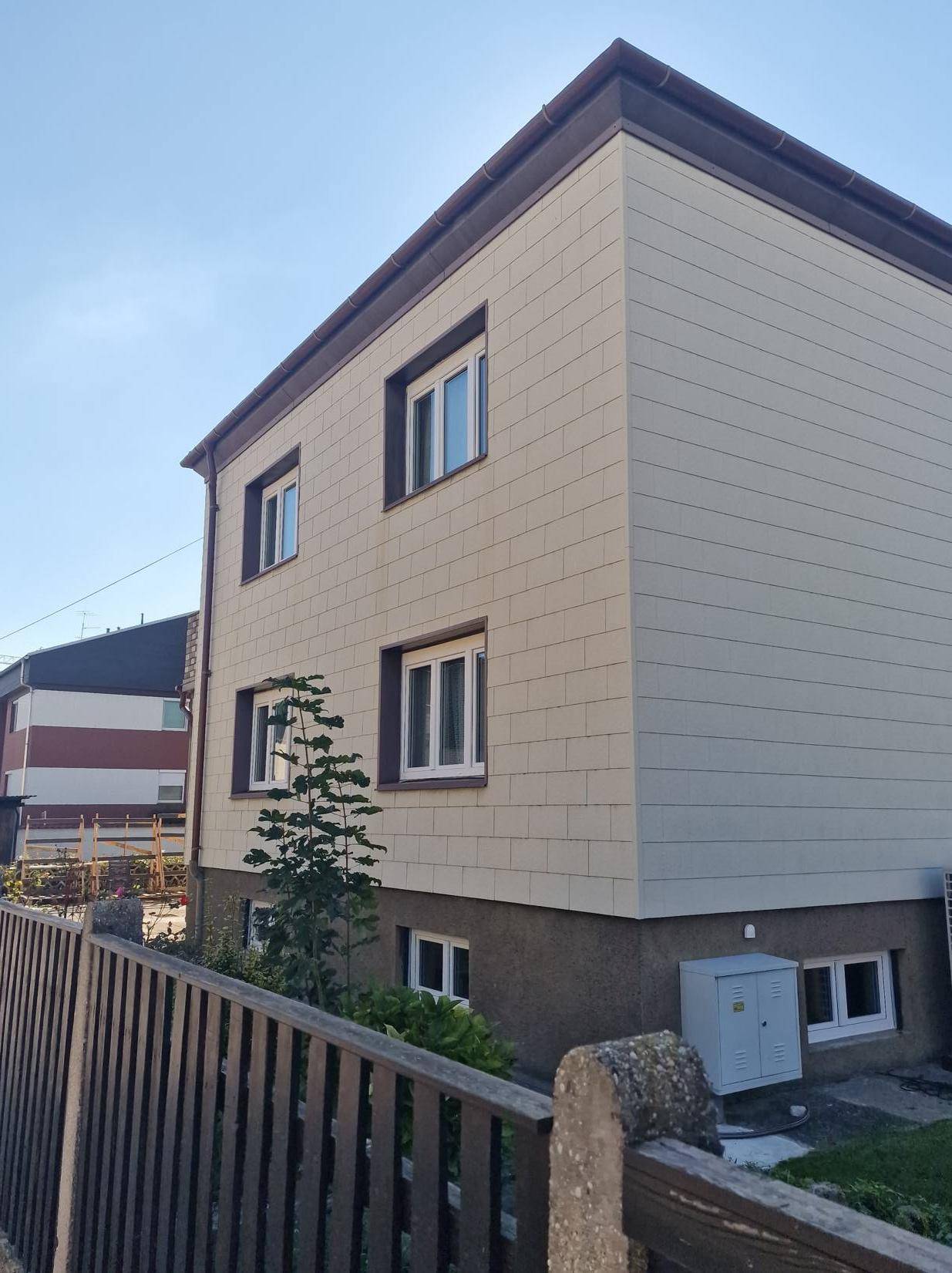 Seitenansicht des Hauses mit heller Fassade und braunen Fensterrahmen.