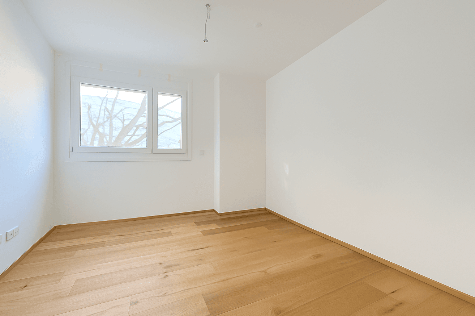 Heller, leerer Wohnraum mit Holzboden und großen Fenstern, die viel Tageslicht hereinlassen.