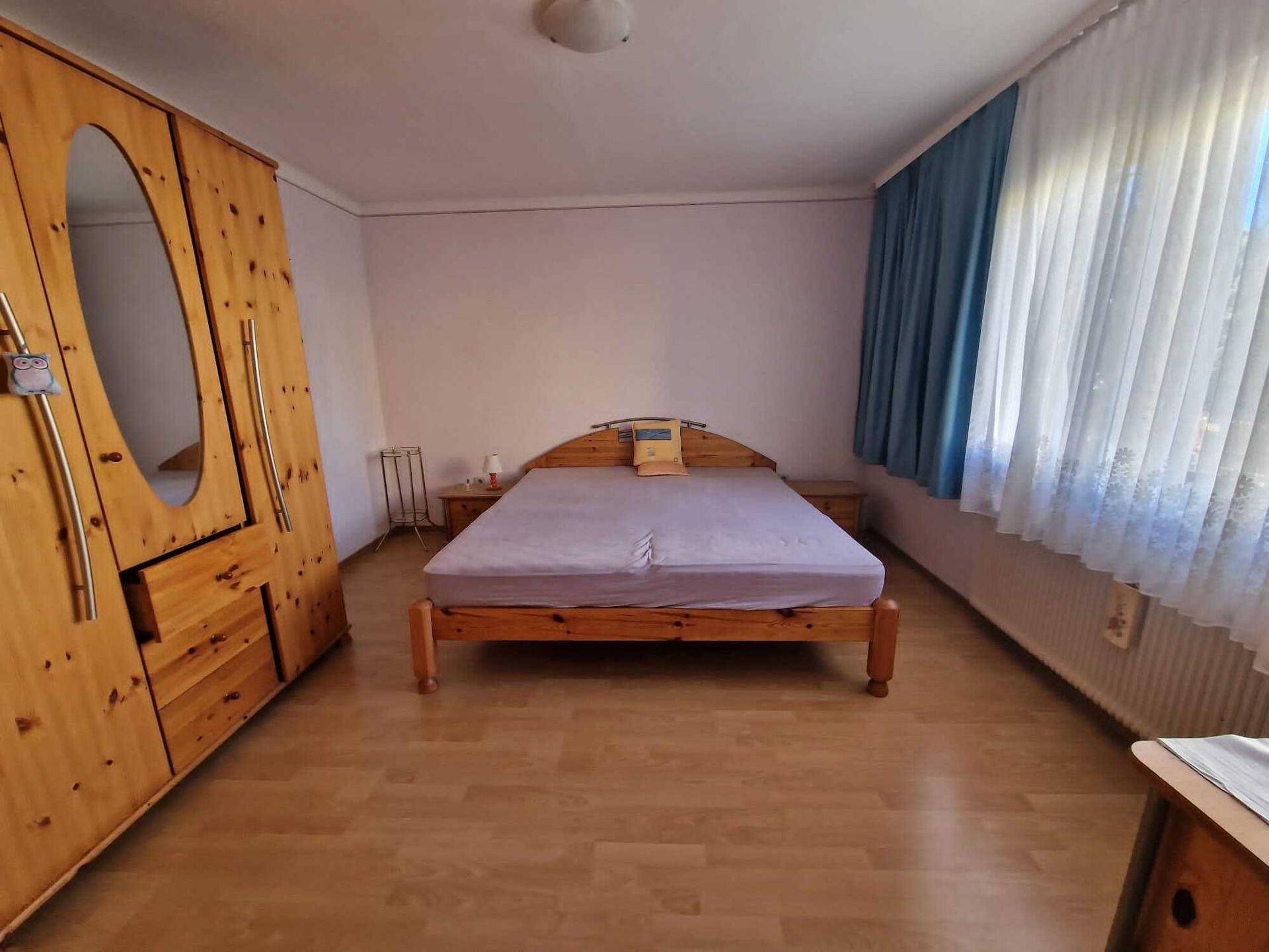 Schlafzimmer mit Laminatboden, Doppelbett und großem Holzschrank.
