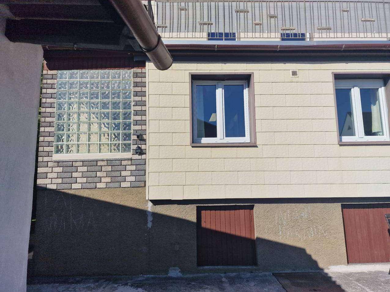 Detailansicht der Hausfassade mit Glasbausteinen und einem Fenster im Erdgeschoss.