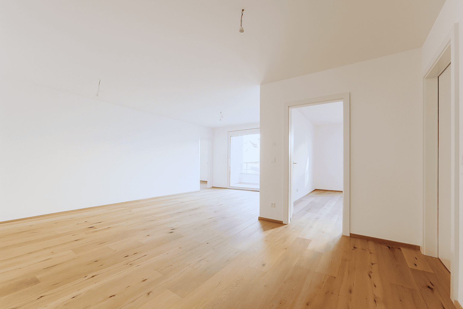 Geräumiger, heller Wohnbereich mit Holzboden und großen Fenstern, bereit zur individuellen Gestaltung.