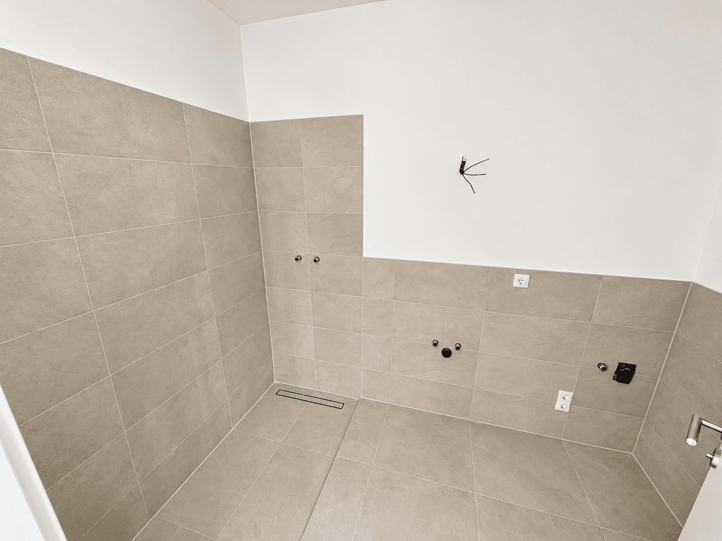 Modern gefliestes Badezimmer mit vorbereiteten Anschlüssen für Dusche und Waschbecken.