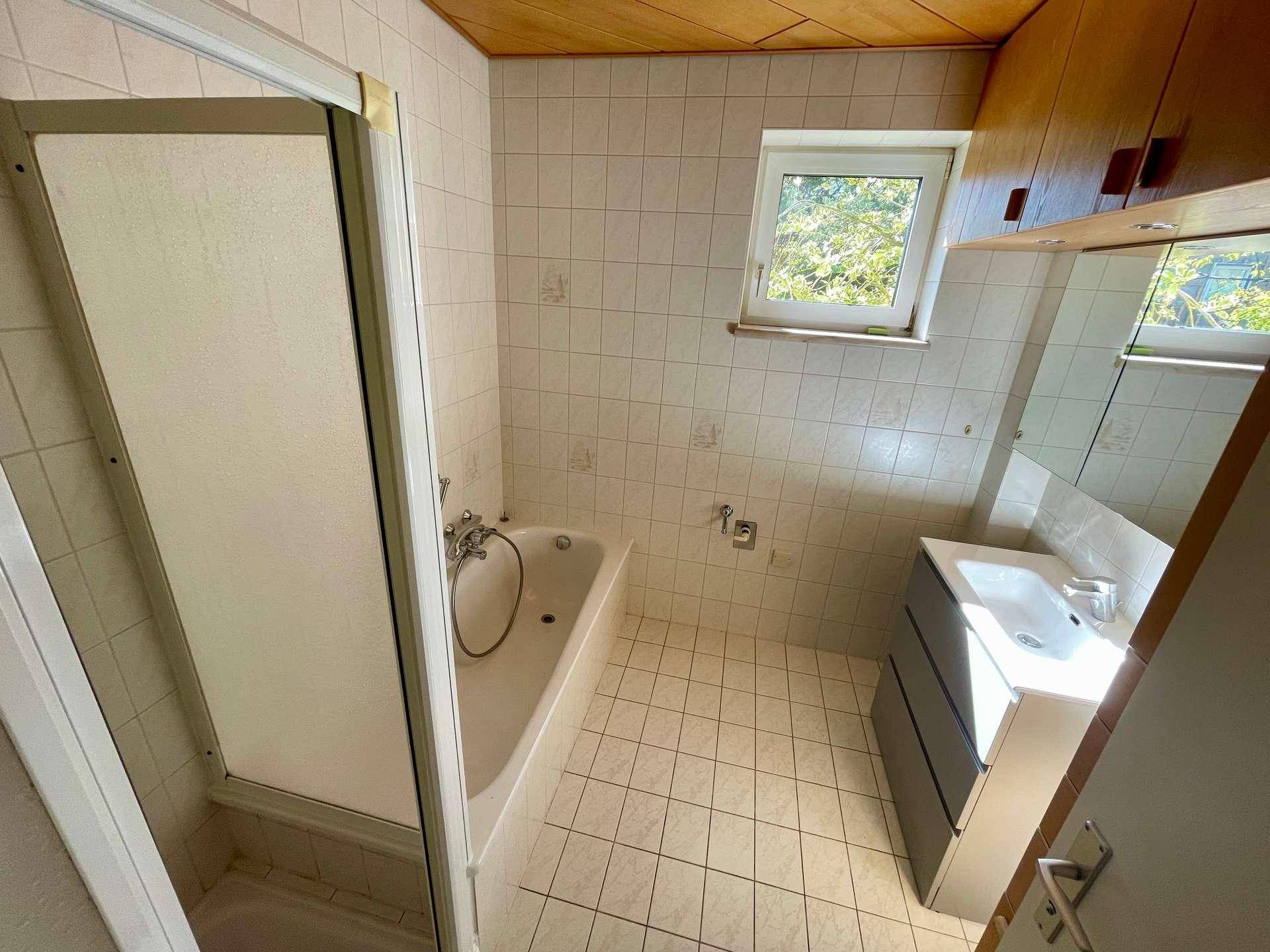 Badezimmer mit Badewanne, Duschkabine, Waschbecken und Fenster.