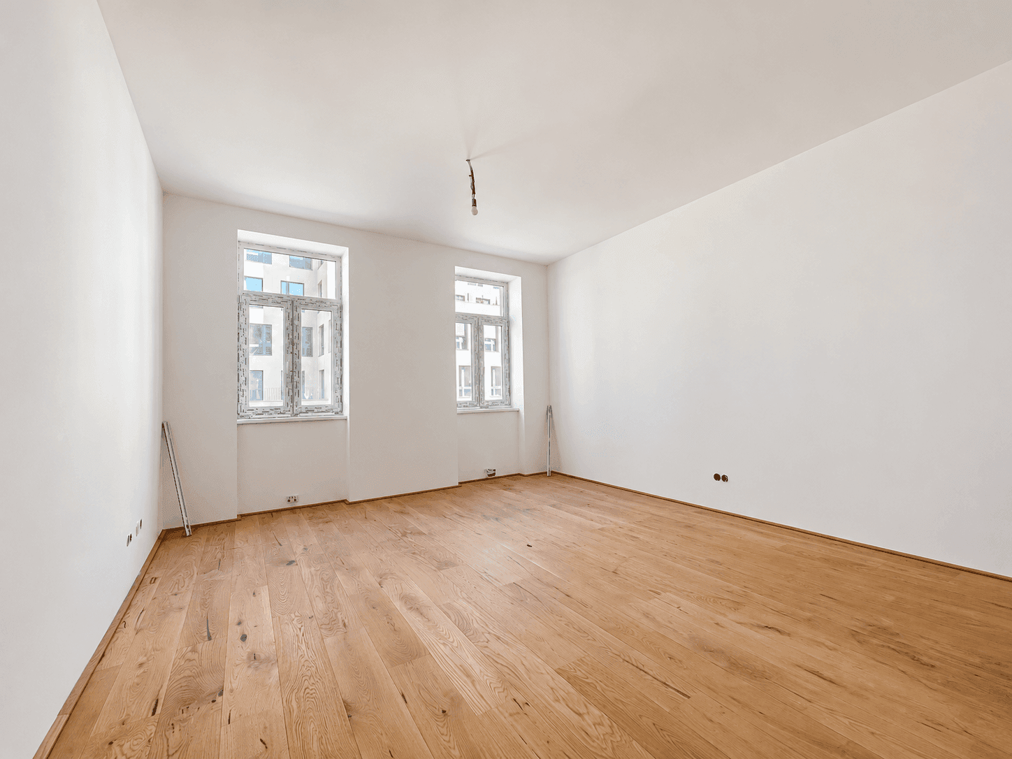 Heller, leerer Raum mit neuem Holzplankenboden und zwei großen Fenstern, ideal als Wohnzimmer.