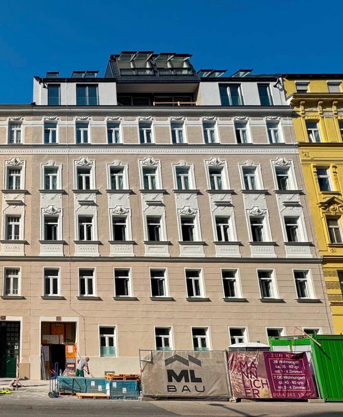 Fassade eines Mehrfamilienhauses mit vielen Fenstern und einem modernen Dachausbau.