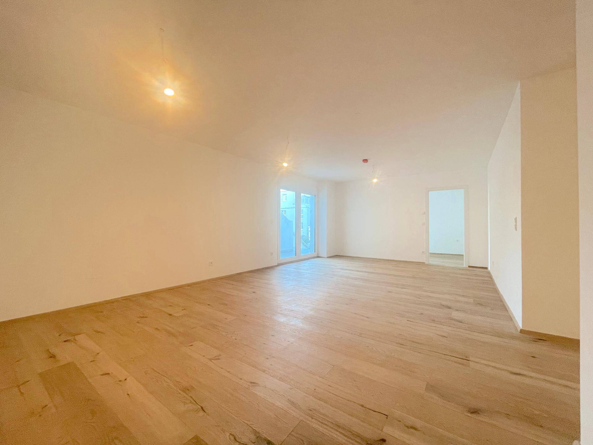 Heller Wohnraum mit Holzboden und großen Fenstern, die viel Tageslicht hereinlassen.