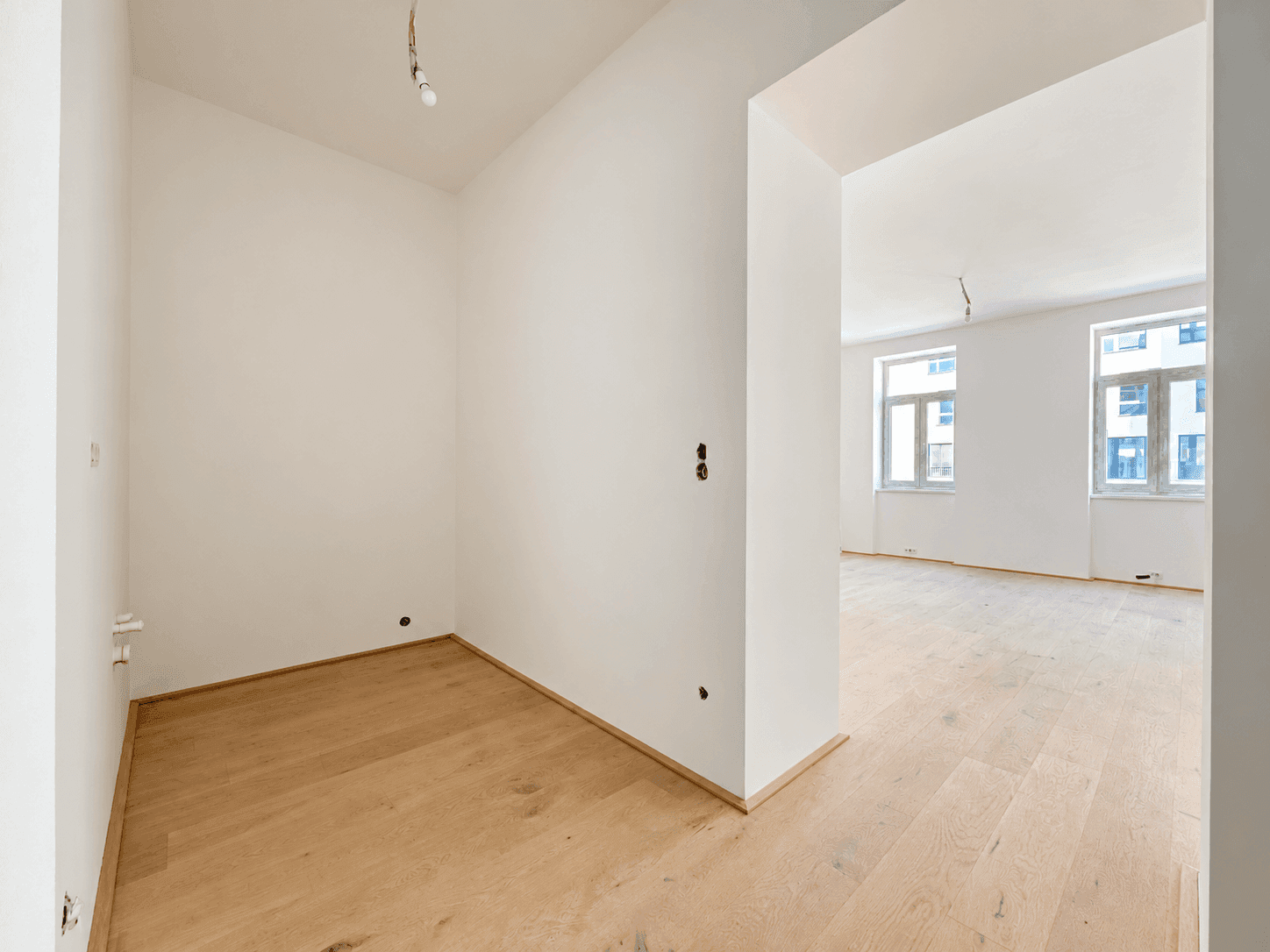 Heller Eckbereich eines Zimmers mit Holzboden und Blick in einen angrenzenden Raum.