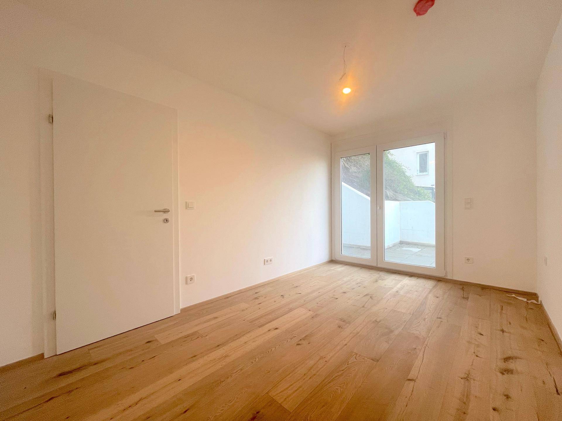Heller Raum mit Holzboden und weißer Tür, ideal als Schlaf- oder Arbeitszimmer.