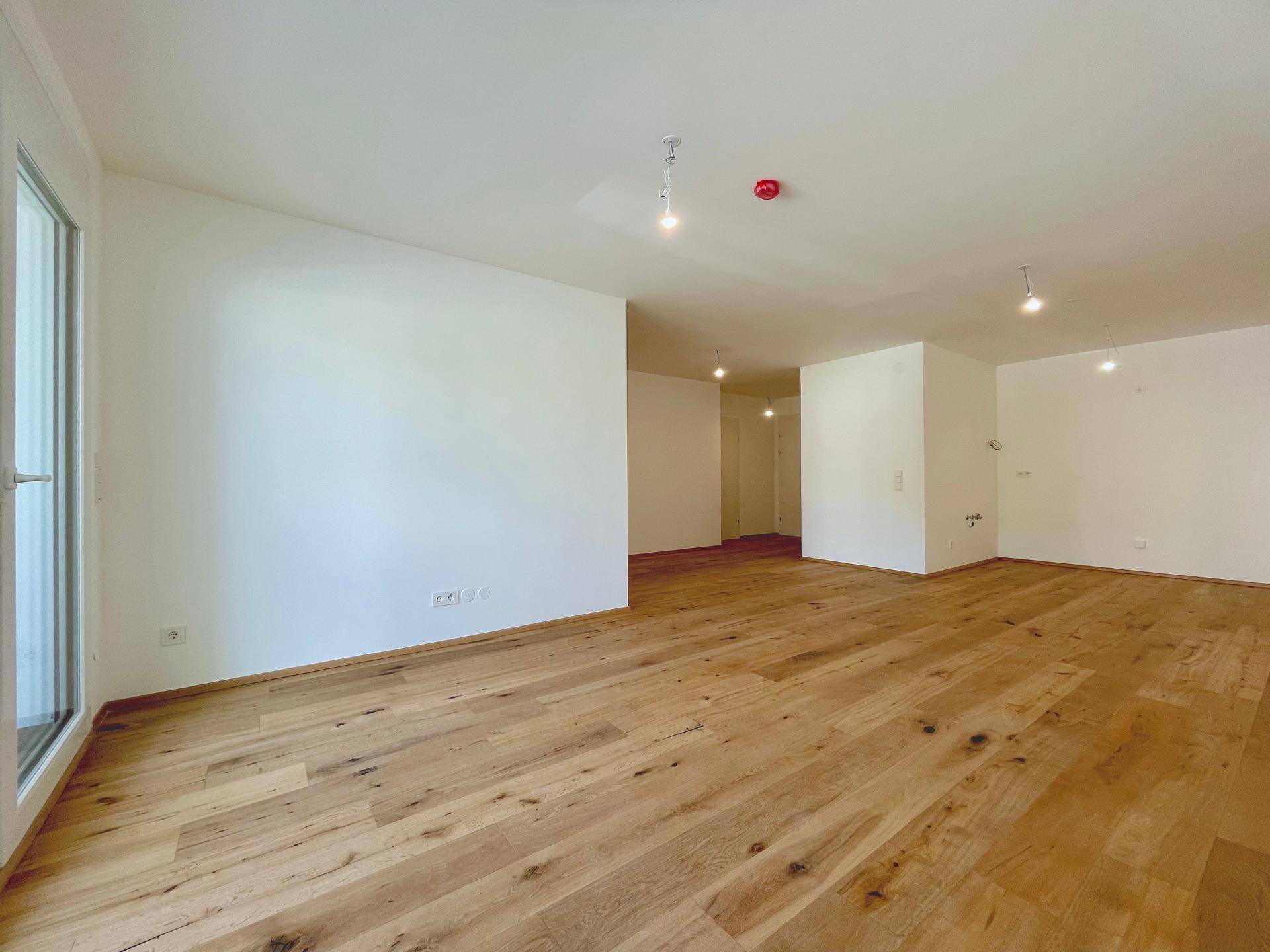 Weitläufiges Wohnzimmer mit hellem Holzboden und weiß gestrichenen Wänden, bietet viel Gestaltungsfreiheit.