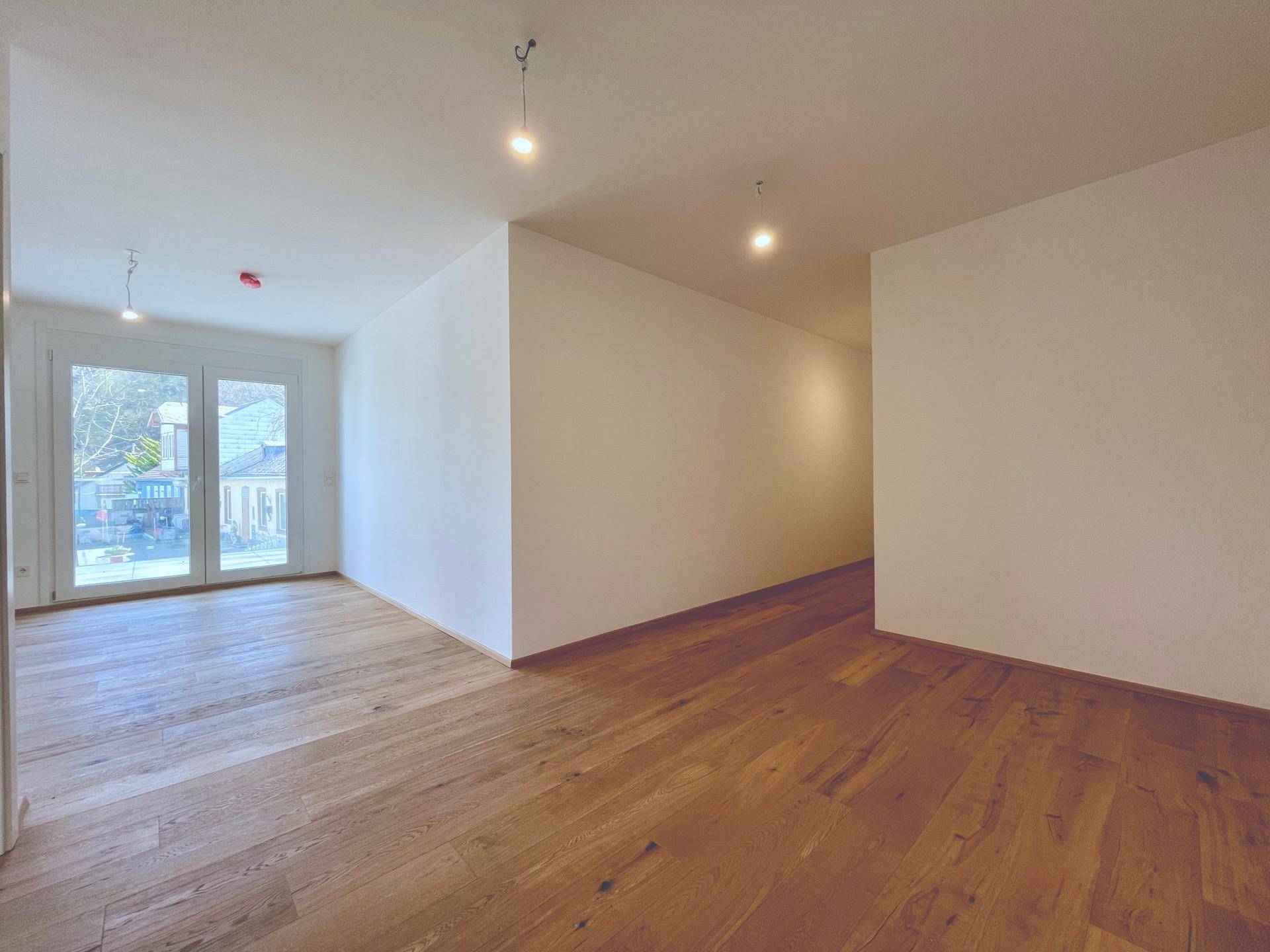 Weitläufiges Wohnzimmer mit hellem Holzboden und weiß gestrichenen Wänden, ideal für offenes Wohnen.