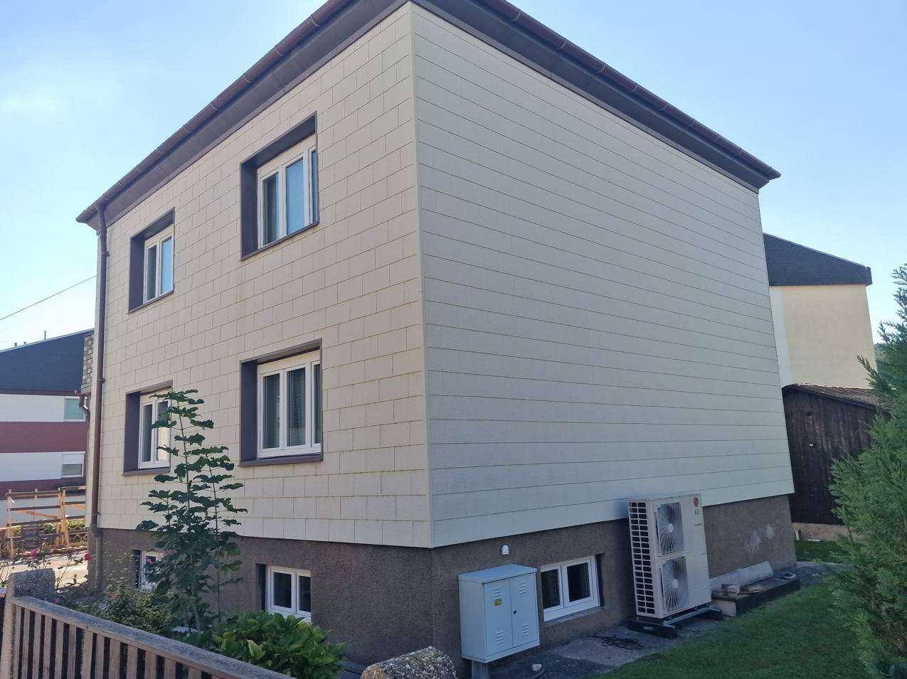 Modernes Wohnhaus mit heller Fassadenverkleidung und Wärmepumpe im Außenbereich.