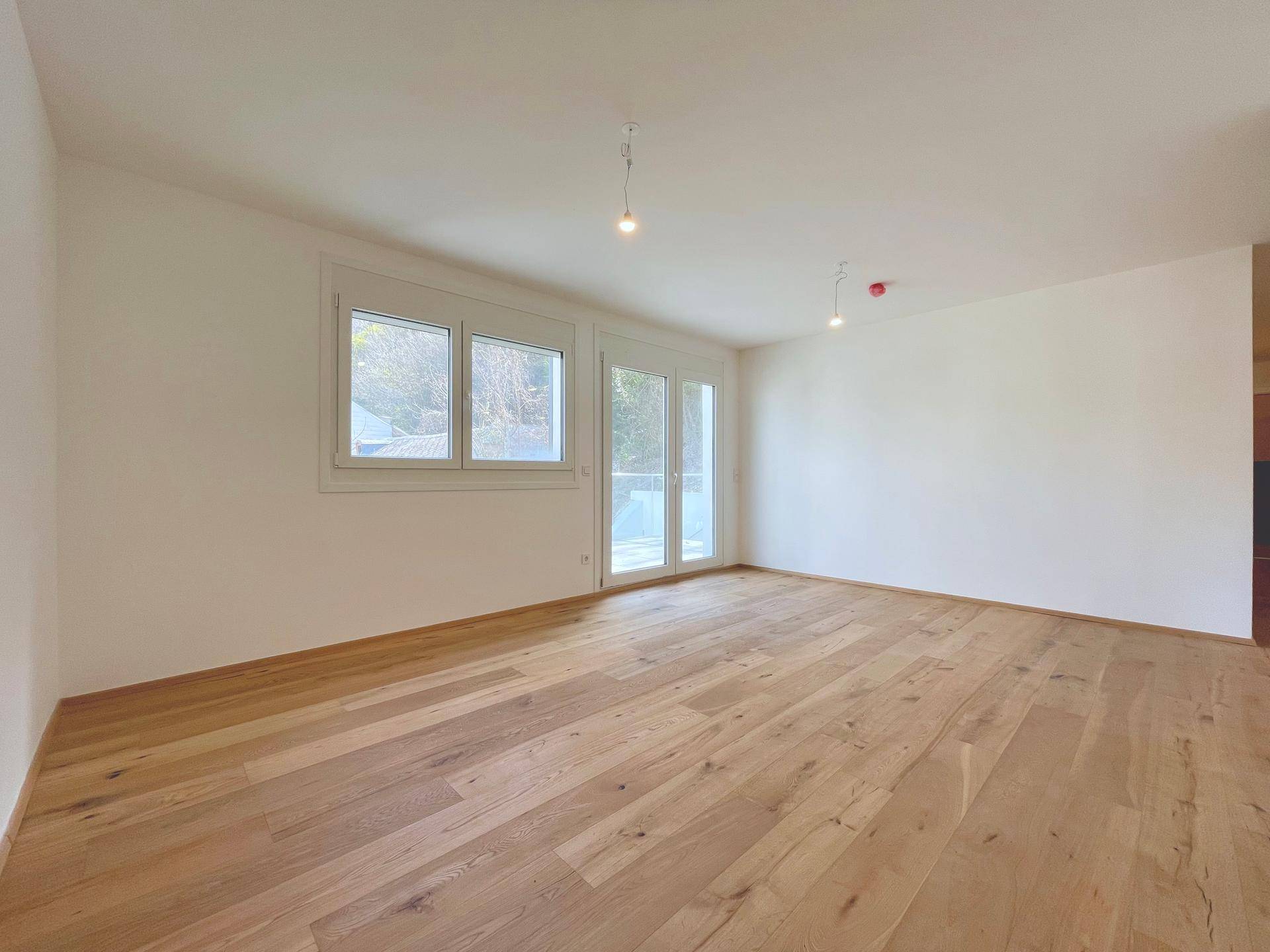 Helles Wohnzimmer mit Holzboden und großen Fenstern, bietet Zugang zu einem Außenbereich.