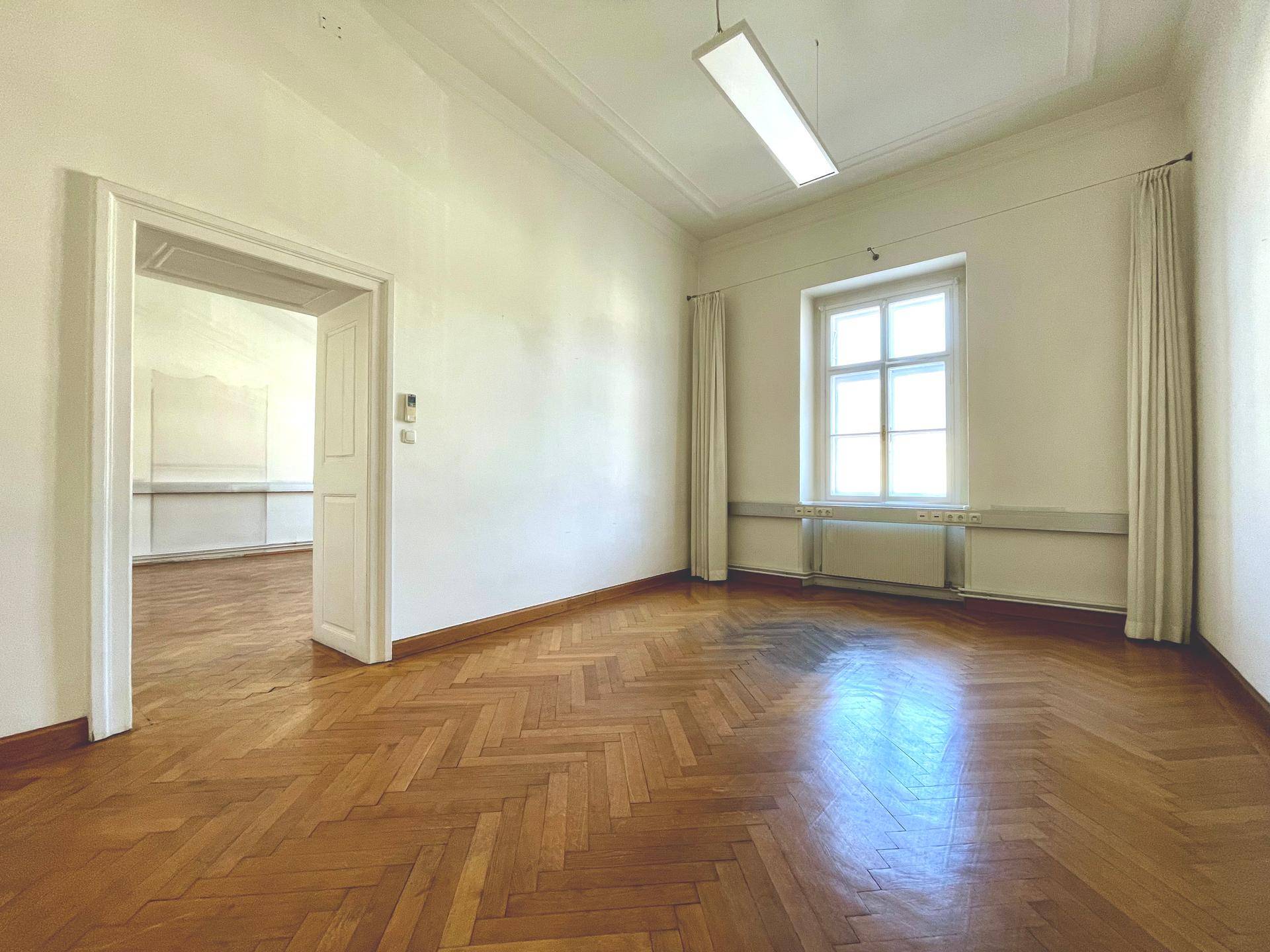 Geräumiger Raum mit klassischem Fischgrätparkett und einem großen Fenster, das viel Licht hereinlässt.