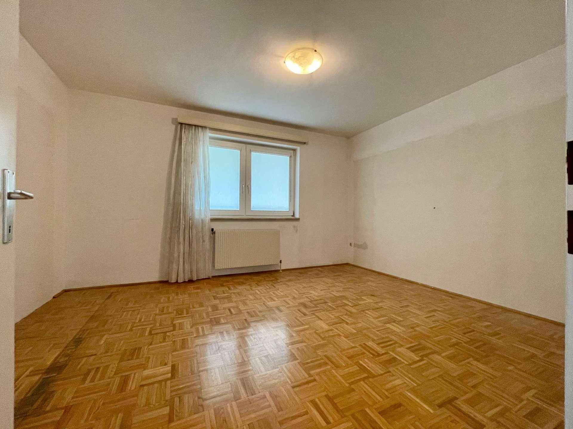 Helles Schlafzimmer mit Parkettboden und Fenster, bereit zur individuellen Gestaltung.