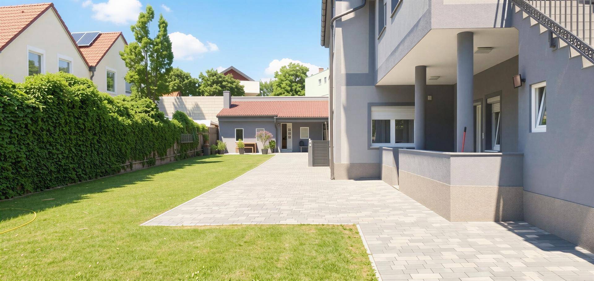 Gepflasterter Weg und Rasenfläche neben dem modernen Gebäude mit hoher Hecke im Hintergrund.