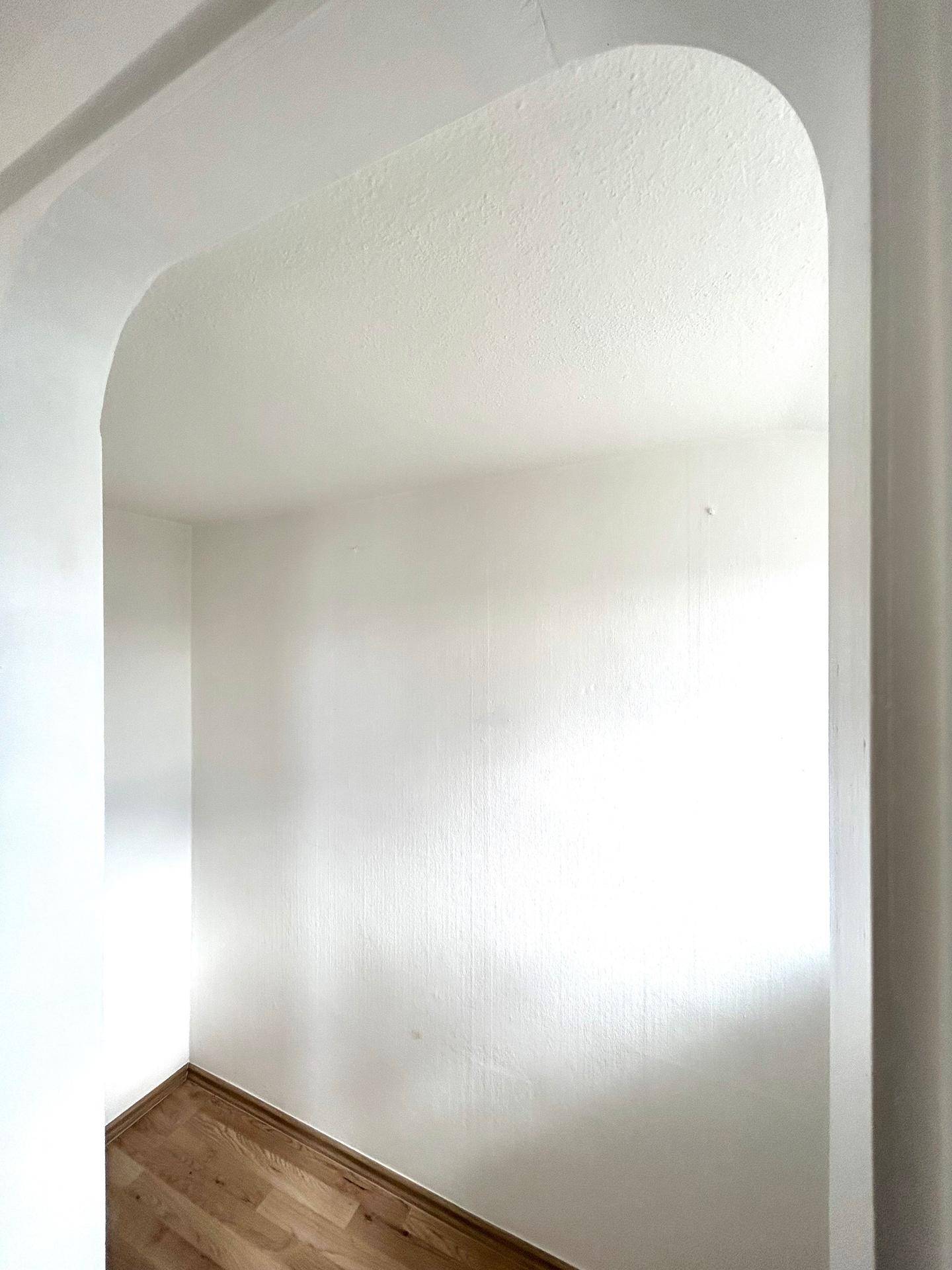Helle Nische mit weiß gestrichenen Wänden und Holzfußboden, ideal als Abstellraum.