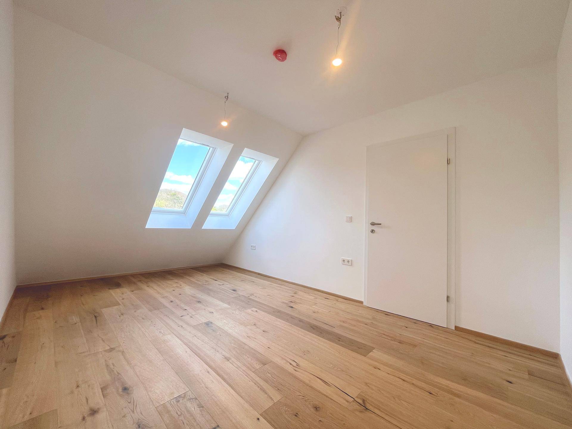 Helles Schlafzimmer im Dachgeschoss mit Holzboden und zwei Dachfenstern, bietet viel Tageslicht.