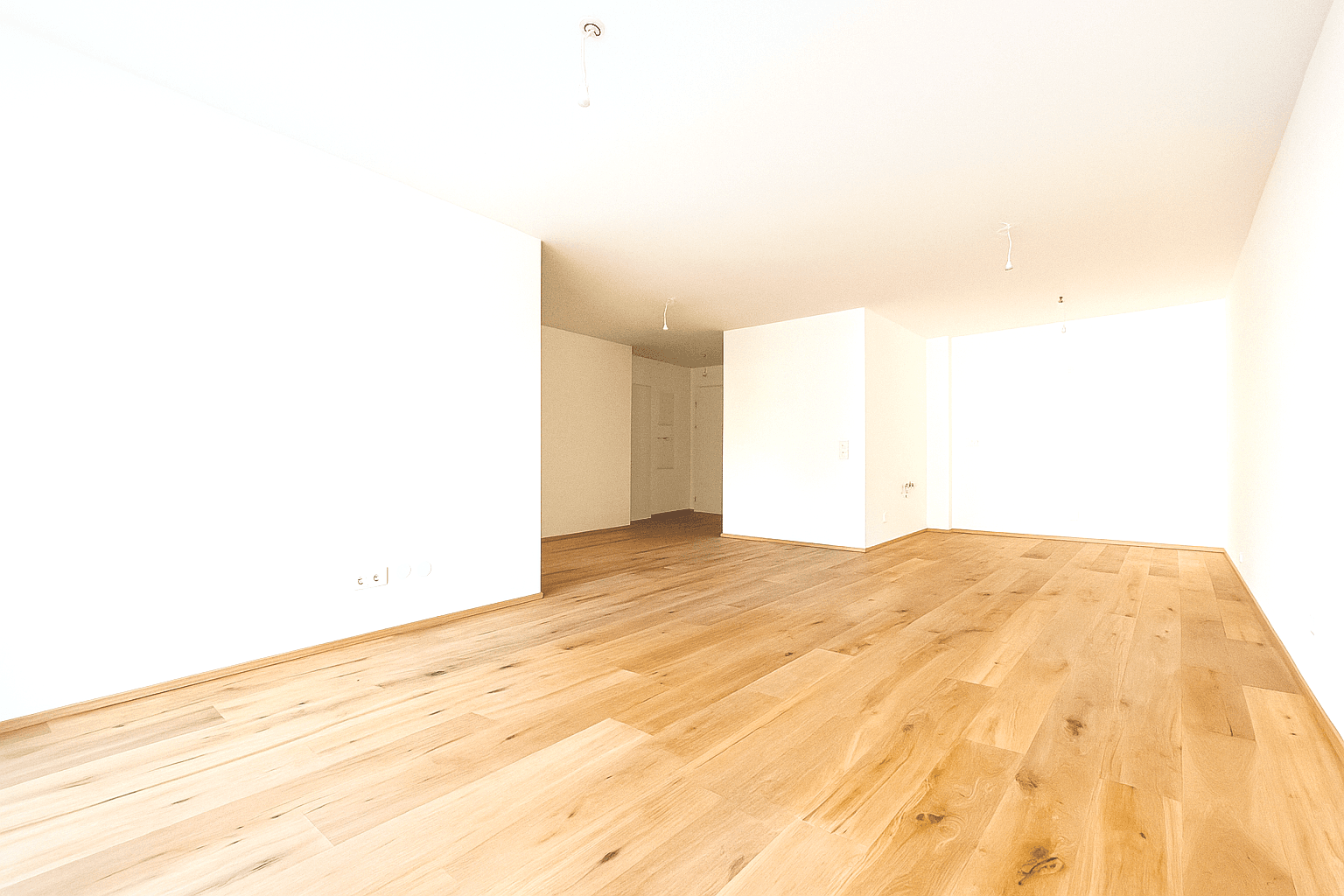 Heller, leerer Wohnraum mit Holzboden und großen Fenstern, die viel Tageslicht hereinlassen.