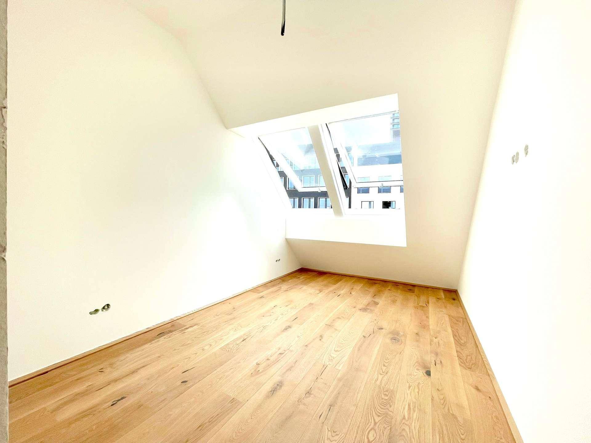 Dachgeschosszimmer mit Holzboden und schrägen Dachfenstern, die für eine helle Atmosphäre sorgen.