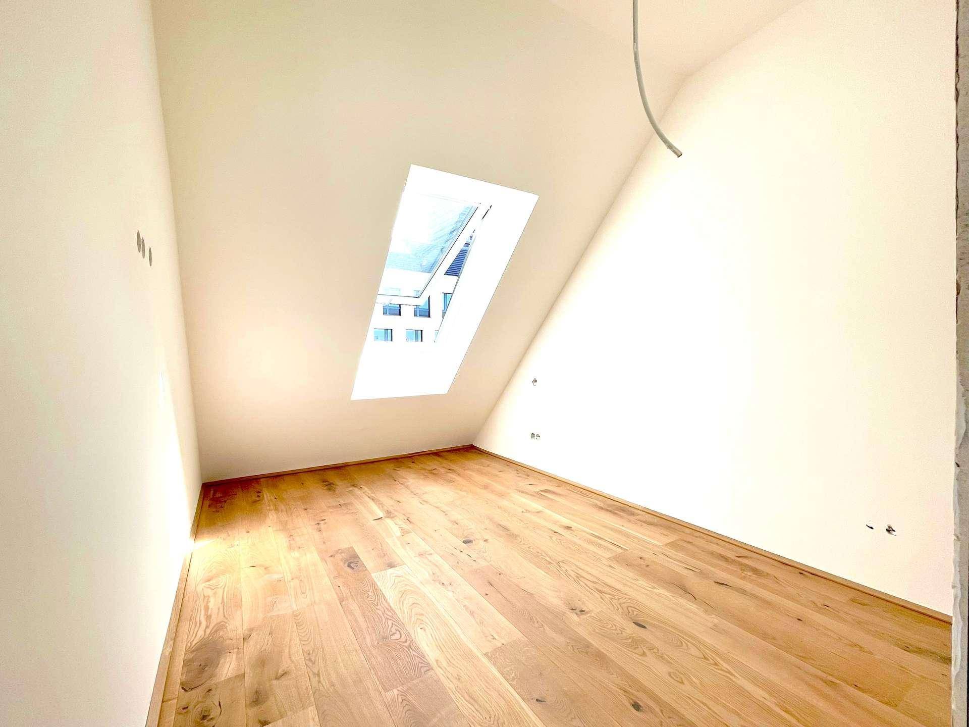 Geräumiges Zimmer mit Holzboden und einem einzelnen Dachfenster, das den Raum erhellt.