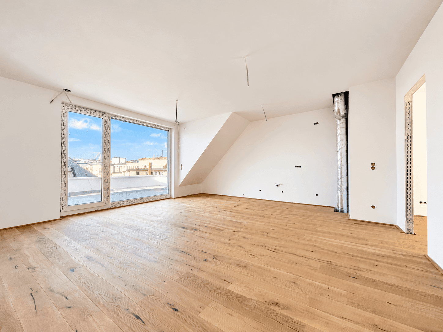 Heller, leerer Wohnraum mit Holzboden und großem Fenster mit Zugang zur Terrasse.