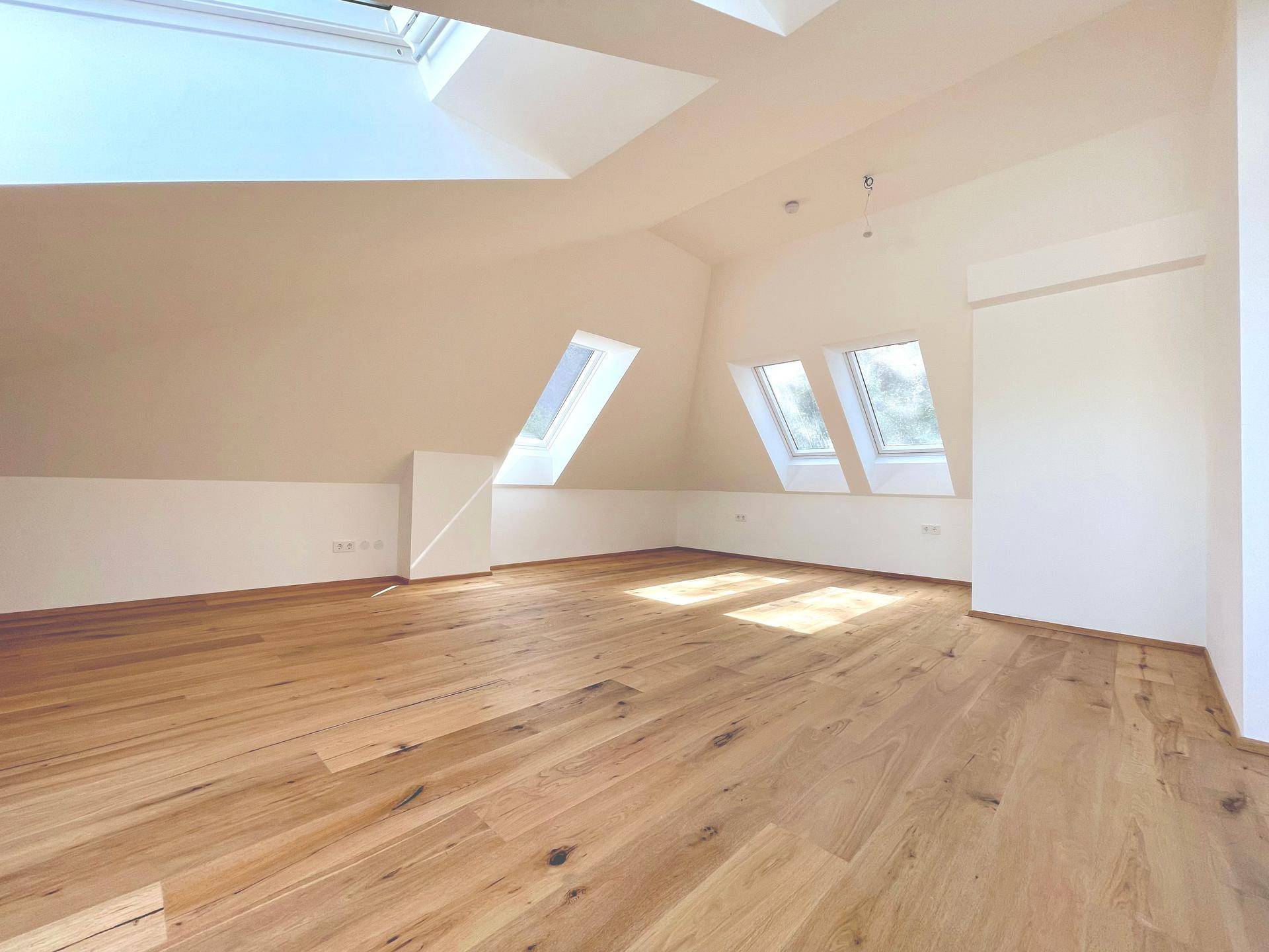 Helles Wohnzimmer im Dachgeschoss mit Holzboden und mehreren Dachfenstern, bietet viel Tageslicht.
