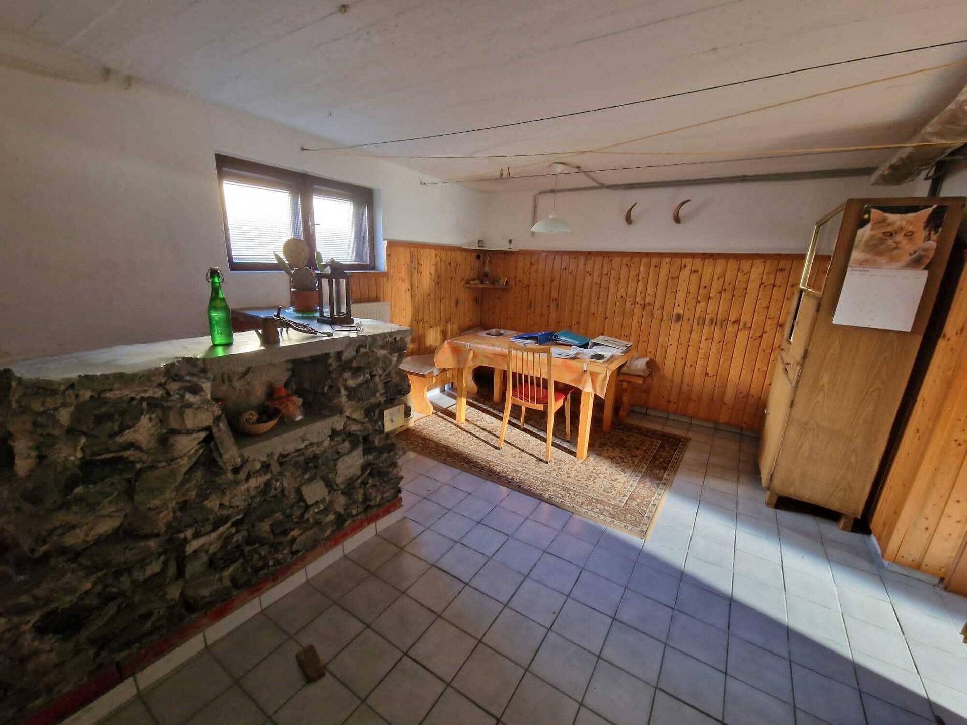 Rustikaler Kellerraum mit Holztäfelung, Steintheke und einem Esstisch.