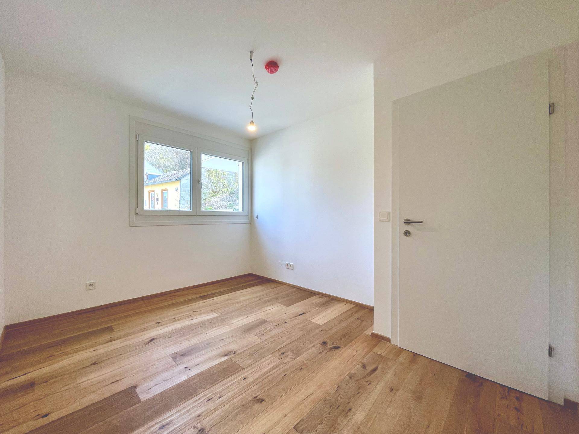 Helles Schlafzimmer mit Holzboden und einem Fenster, bereit zur individuellen Gestaltung.