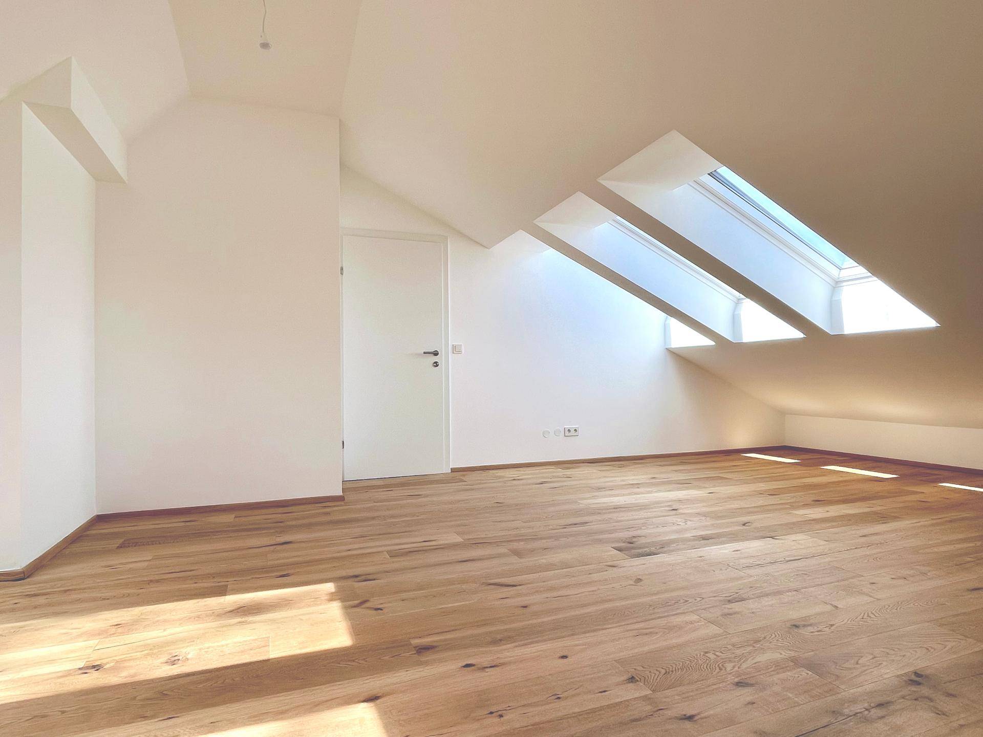 Geräumiges Zimmer im Dachgeschoss mit Holzboden und viel Tageslicht durch die schrägen Dachfenster.