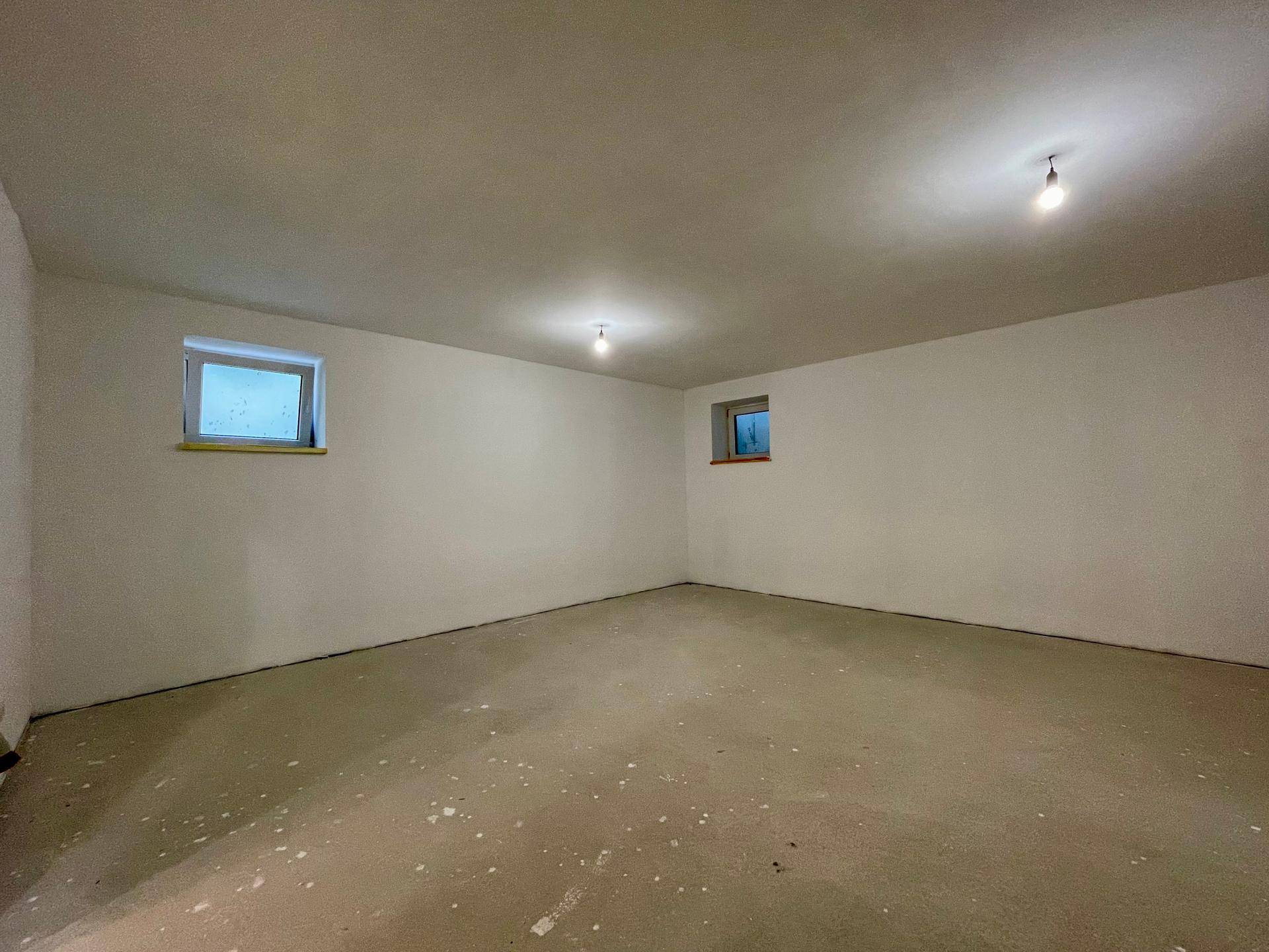 Geräumiger Kellerraum im Rohbau mit kleinen Fenstern und Betonboden.