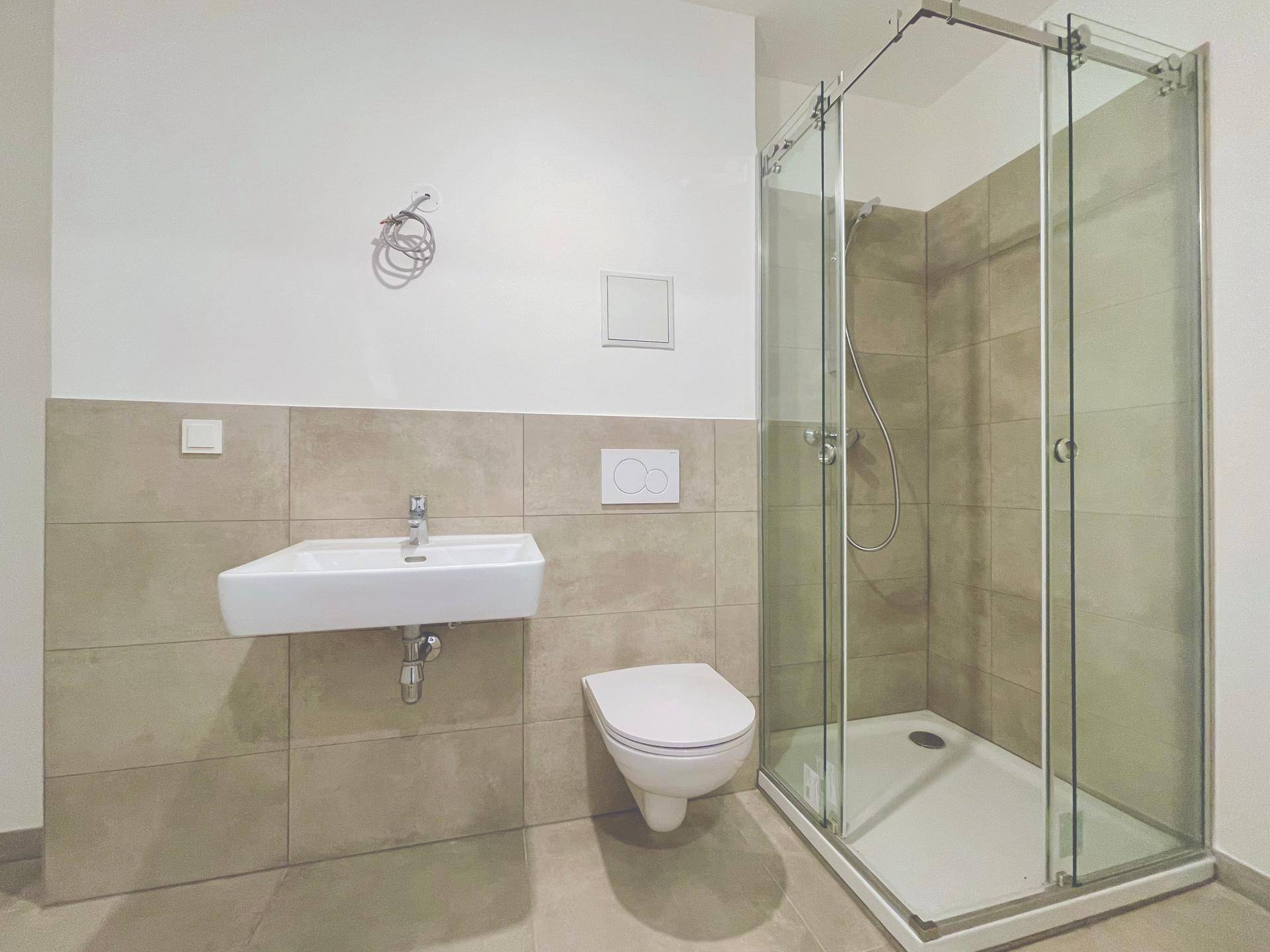Modernes Badezimmer mit Duschkabine, Wand-WC und Waschbecken, ausgestattet mit beigefarbenen Fliesen.