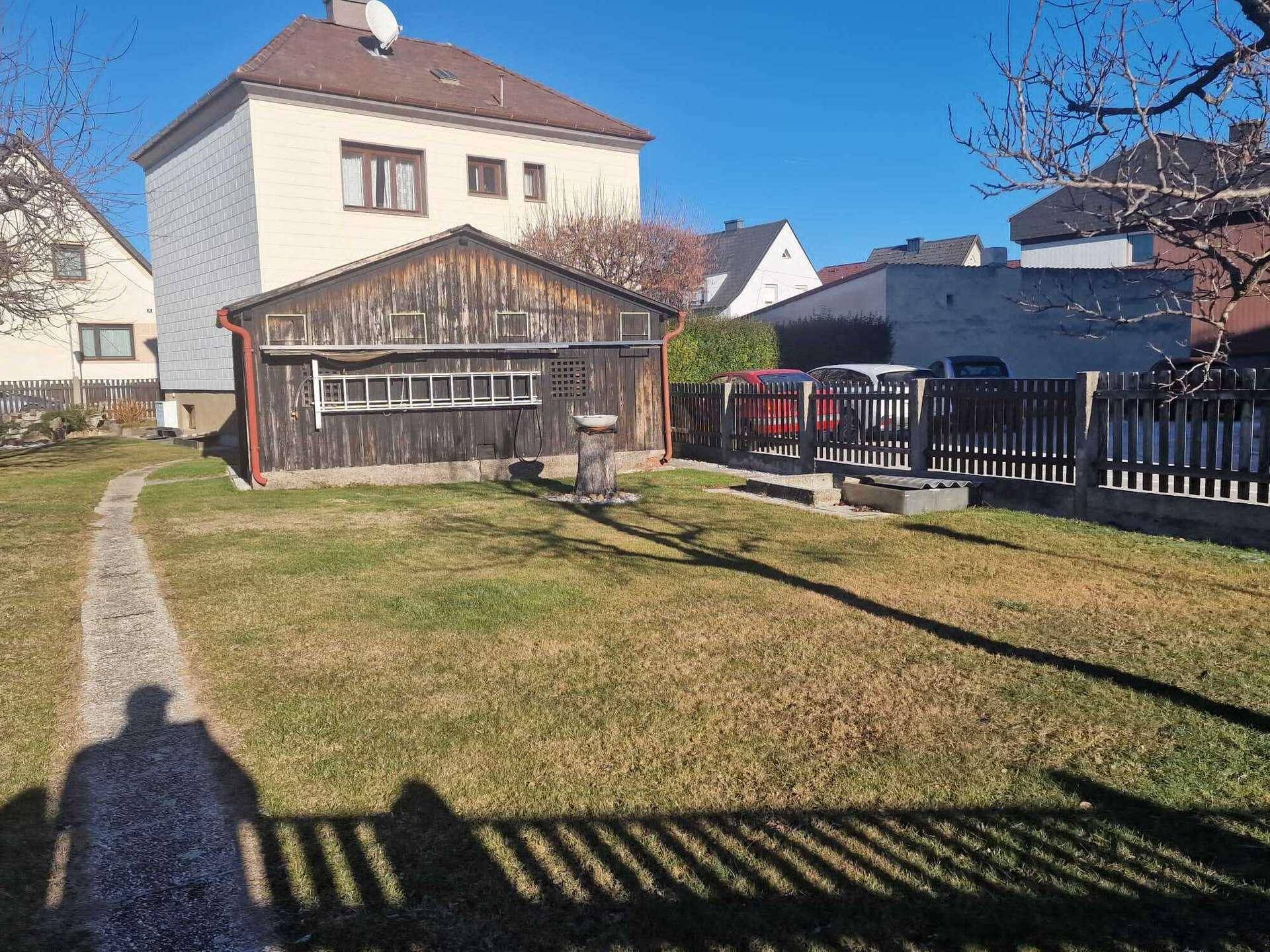Sonniger Gartenbereich mit einem rustikalen Holzschuppen und einem gepflegten Rasen.