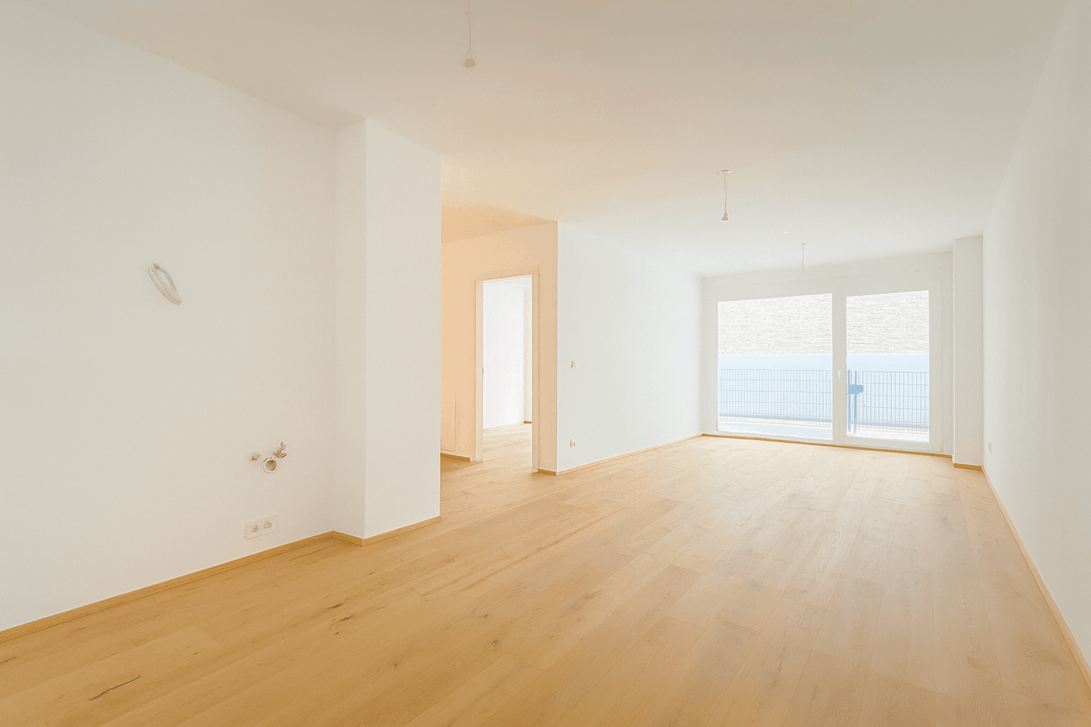 Heller, leerer Wohnraum mit Holzboden und großen Fenstern, die viel Tageslicht hereinlassen.