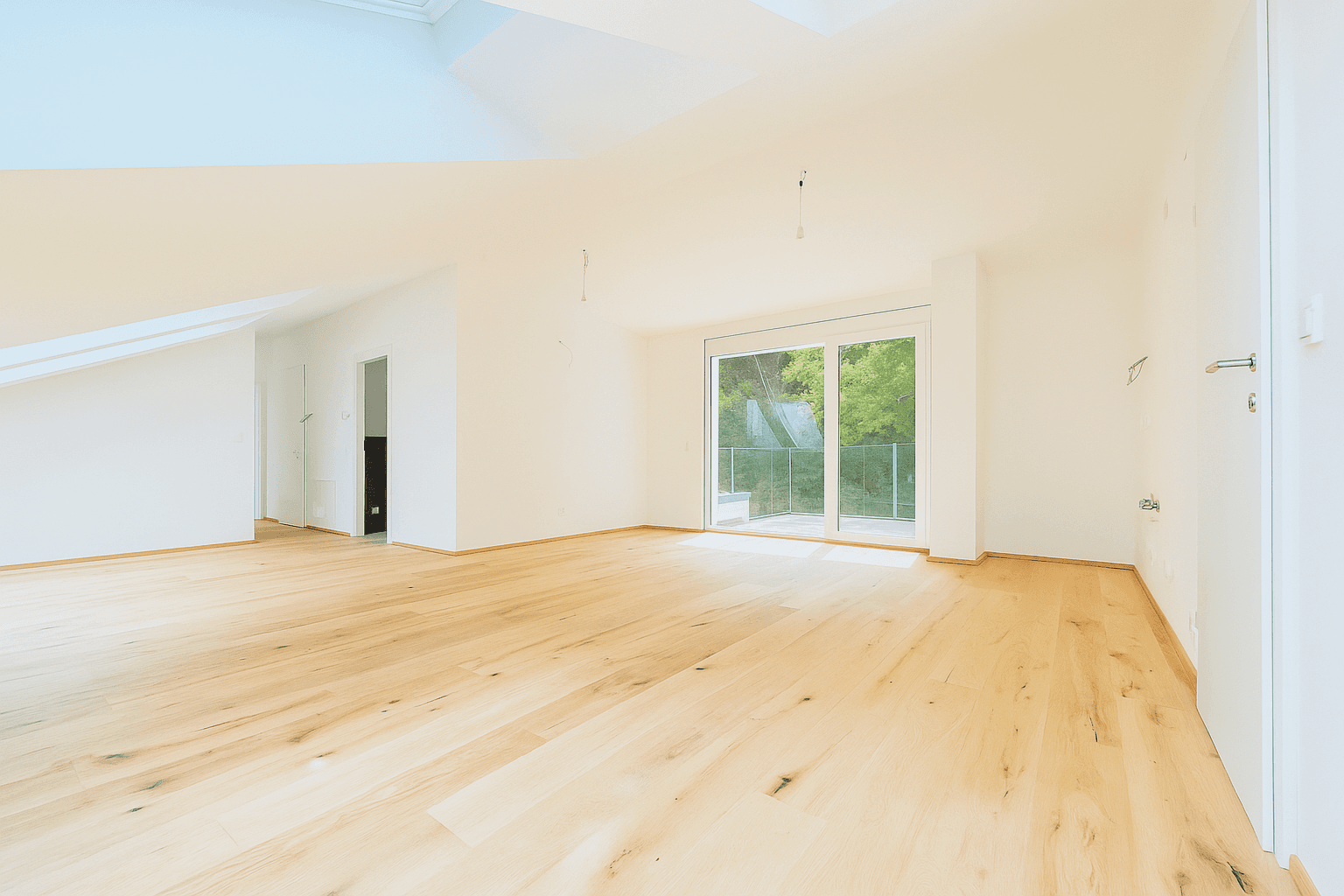 Heller, leerer Raum im Dachgeschoss mit Holzboden und Zugang zu einem Balkon, umgeben von Natur.