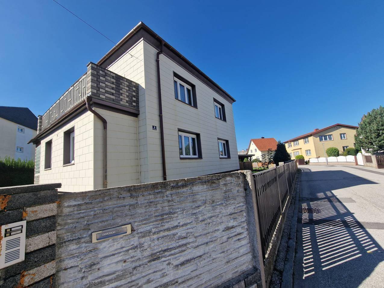 Ansicht des Hauses von der Straße mit heller Fassade und einer Dachterrasse.