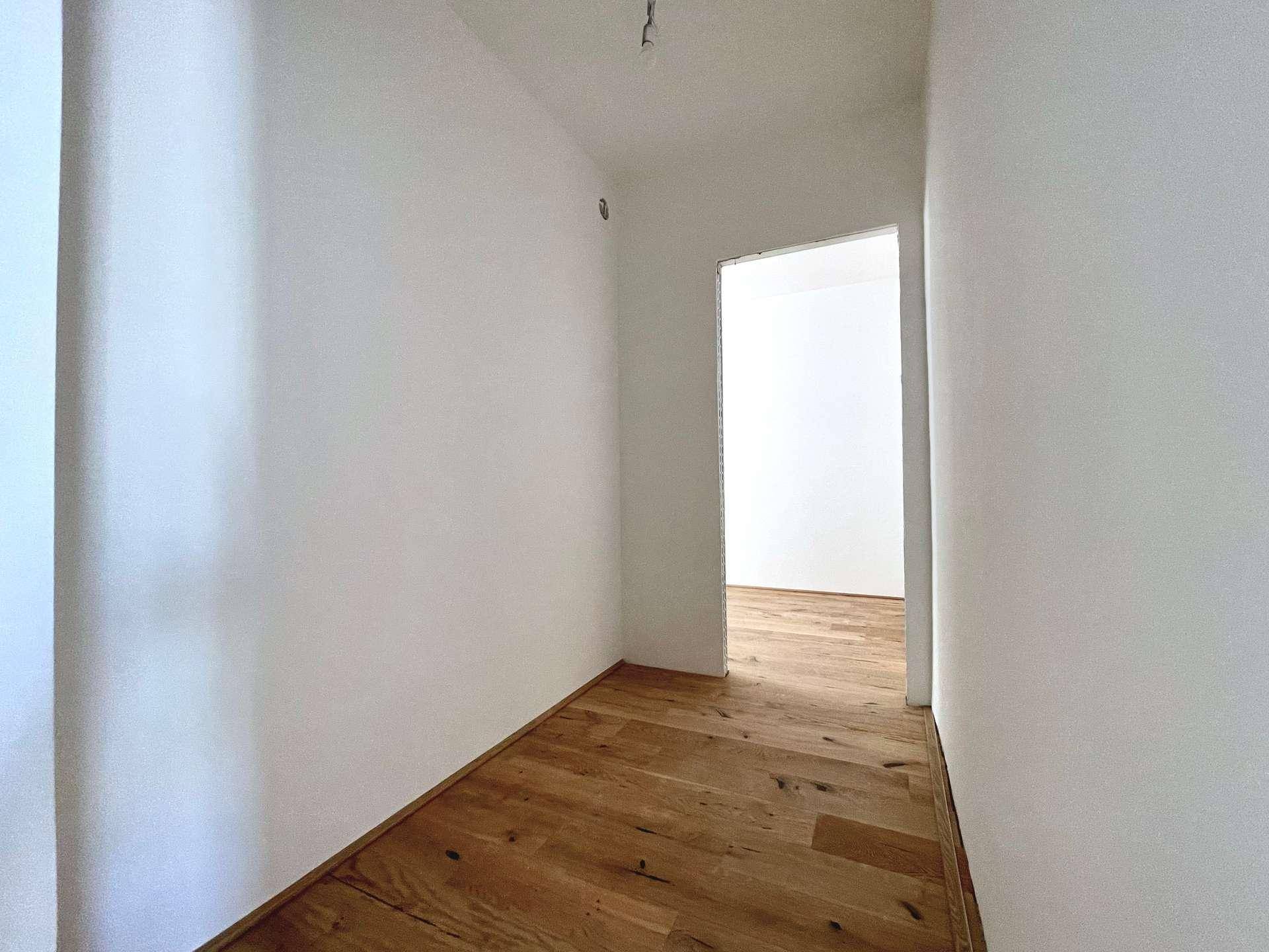 Heller Flur mit Holzboden und weißen Wänden, der zu weiteren Räumen führt.
