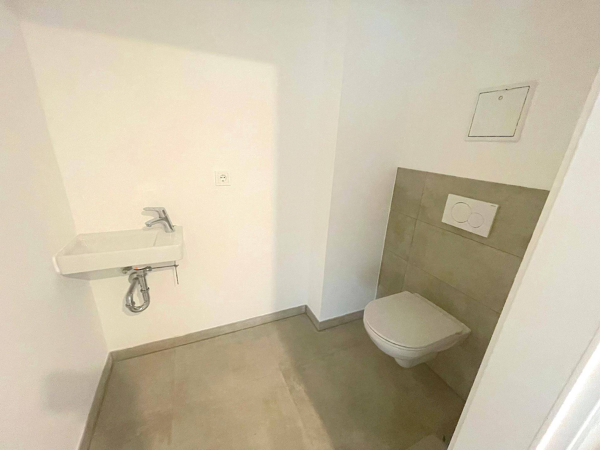 Separates Gäste-WC mit Wand-WC und kleinem Waschbecken, modern gefliest.