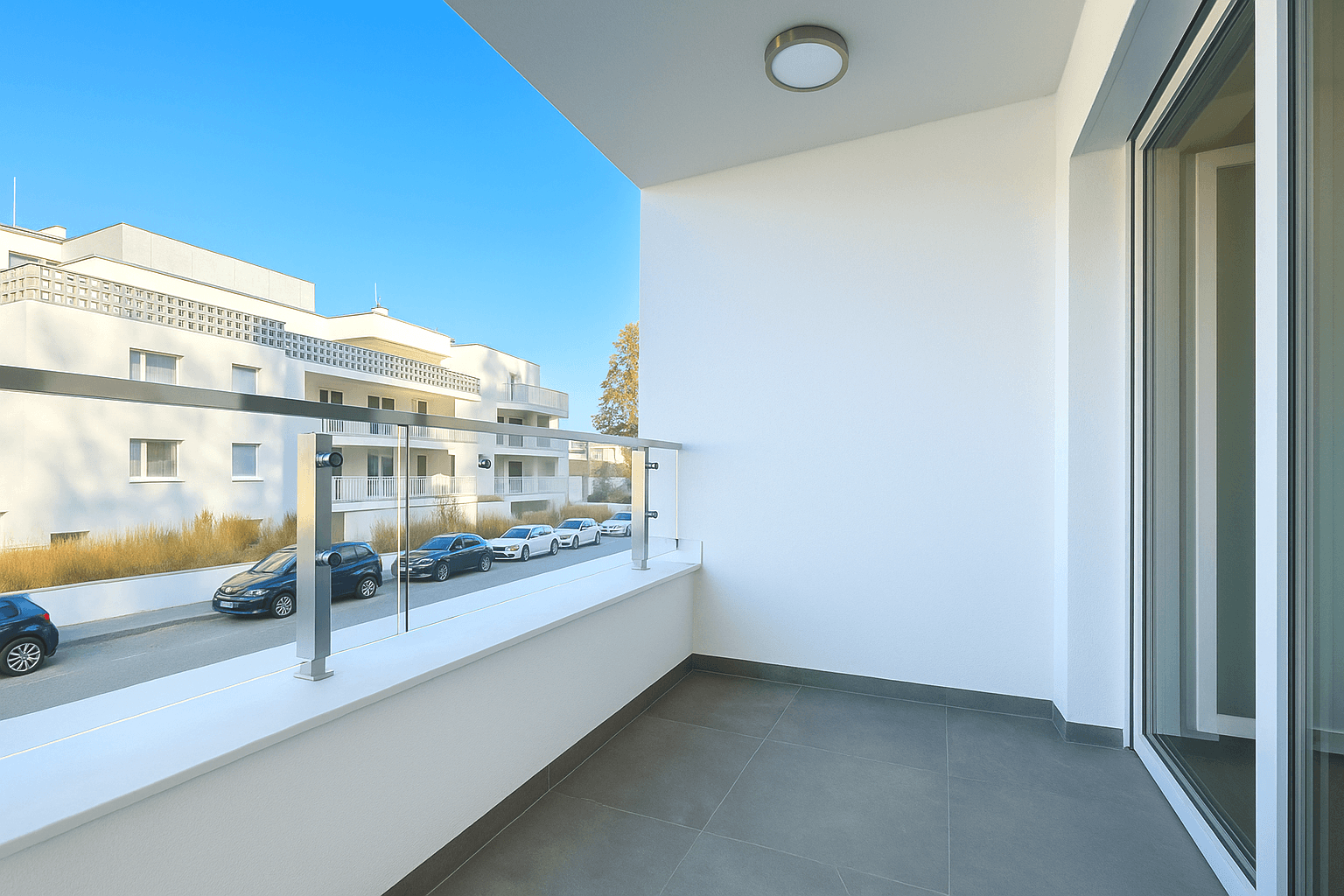Moderner Balkon mit Glasgeländer und Blick auf die Straße und umliegende Gebäude.