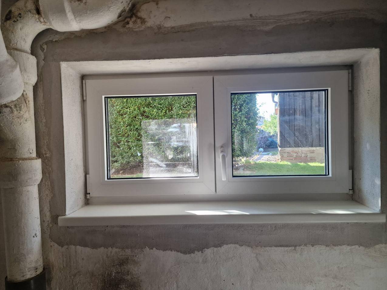Kleines Kellerfenster mit Blick auf den grünen Gartenbereich.