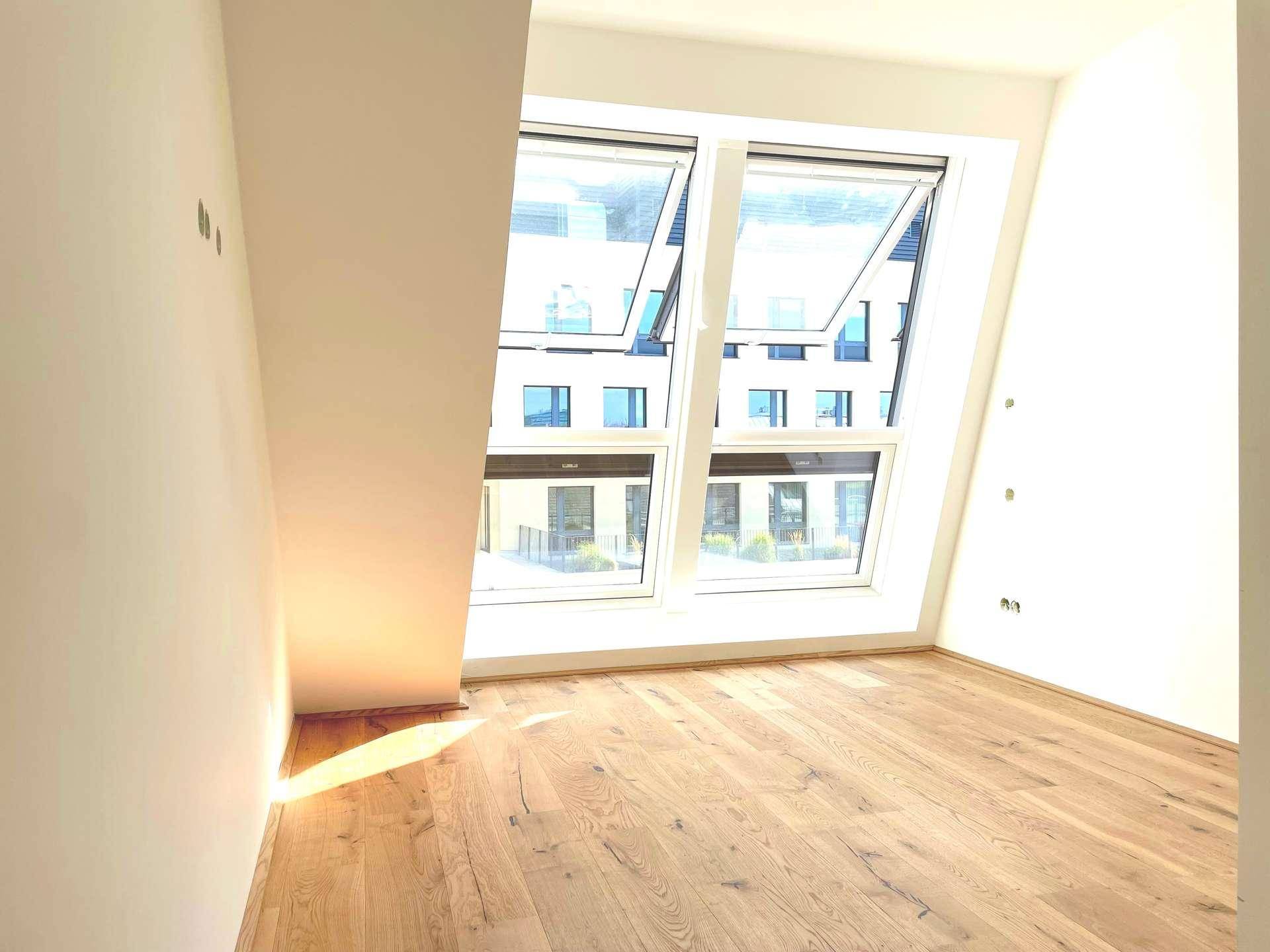 Helles Zimmer mit großen Fenstern und Holzboden, bietet einen Blick auf moderne Gebäude.