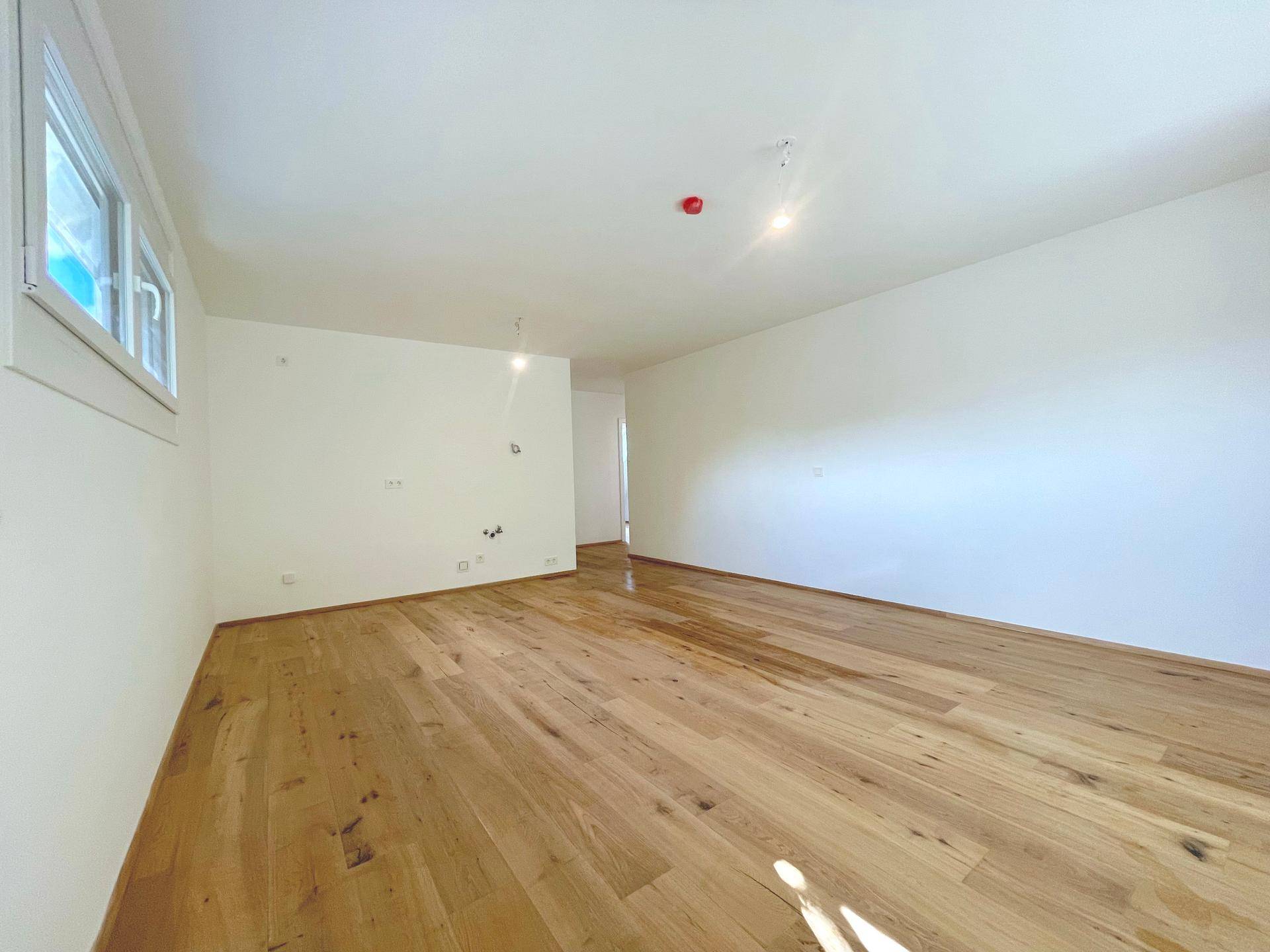 Weitläufiges Wohnzimmer mit hellem Holzboden und weiß gestrichenen Wänden, bereit zur individuellen Gestaltung.
