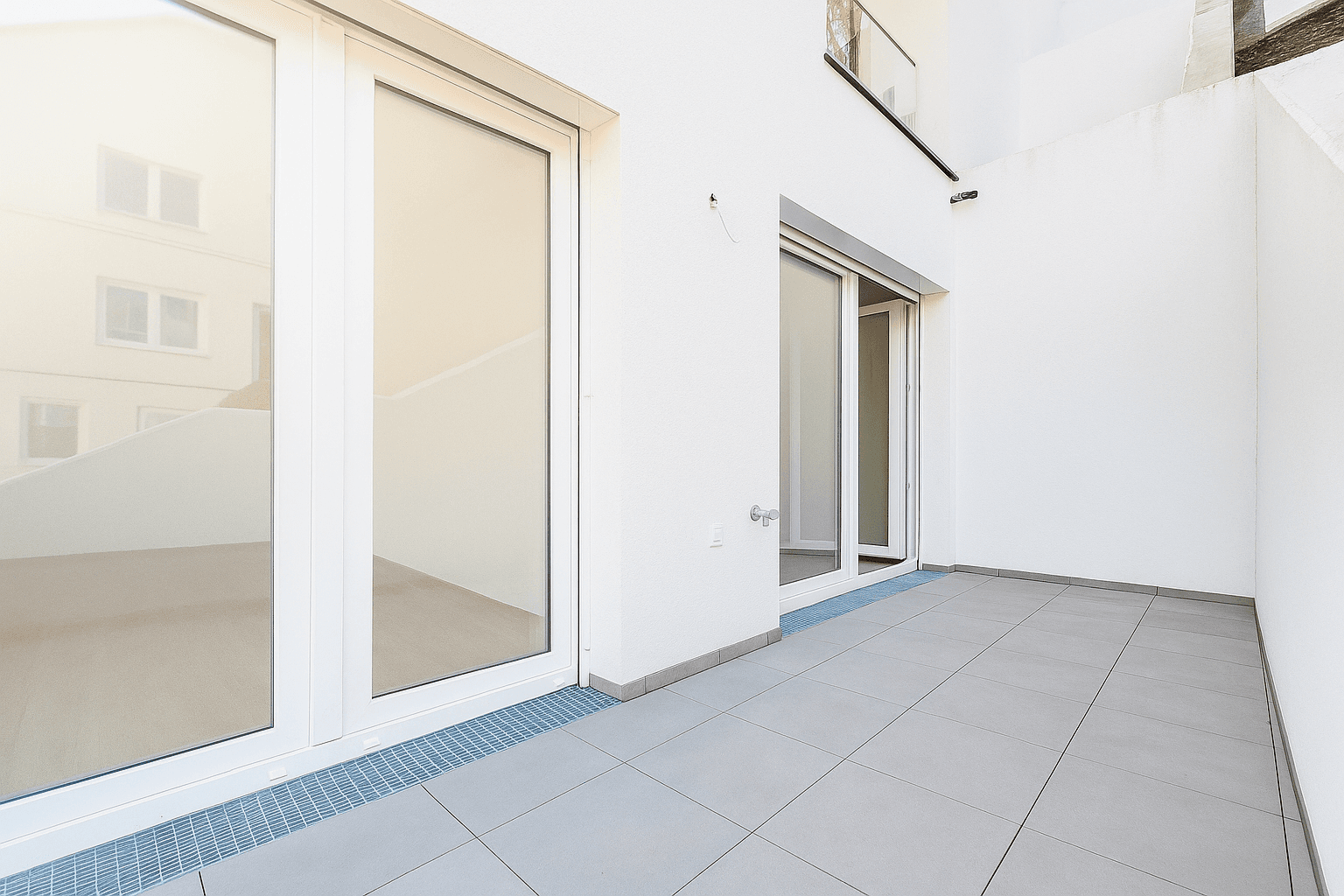 Geräumige Terrasse mit Fliesenboden und weißer Fassade, bietet Platz für Outdoor-Möbel.