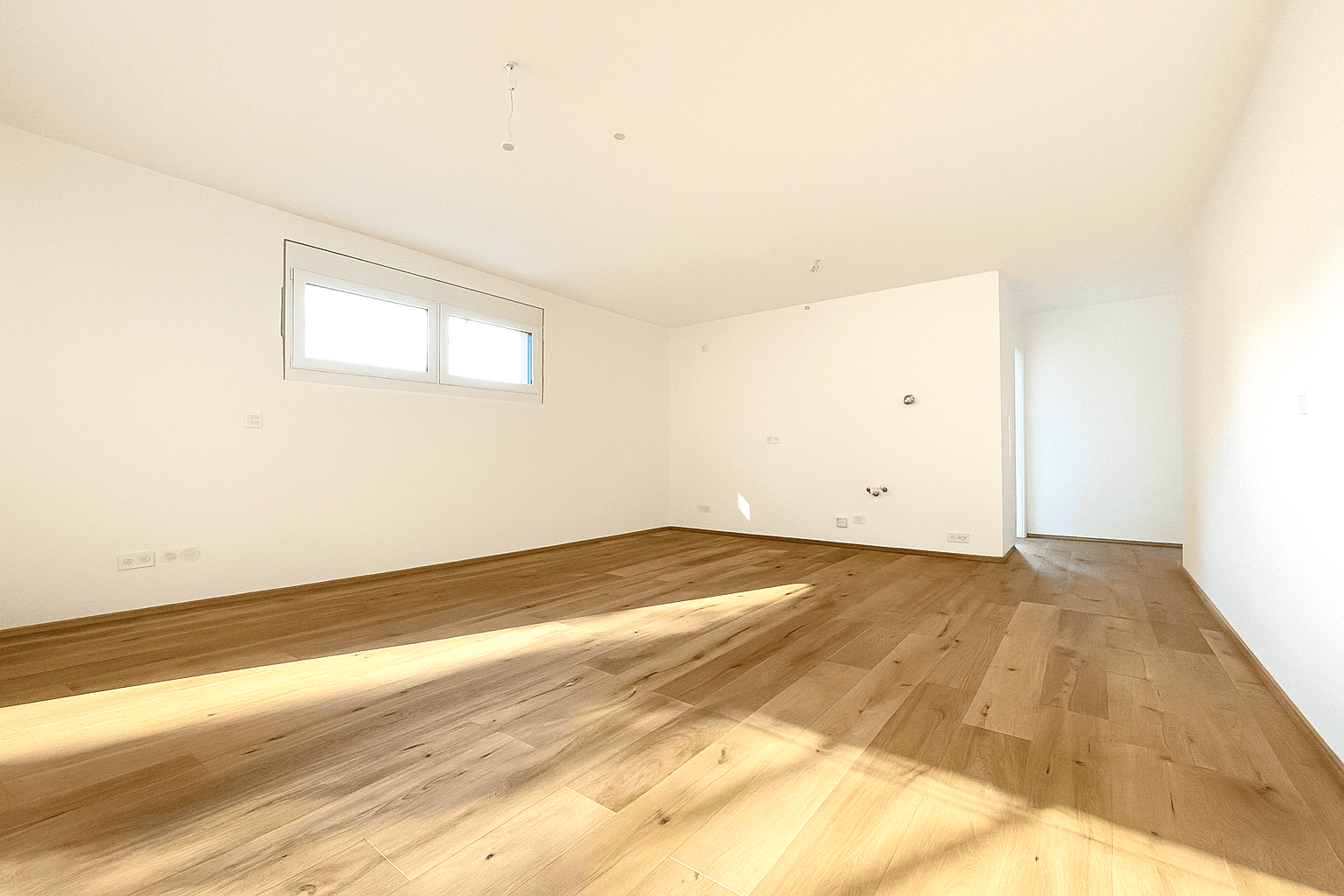 Heller, leerer Wohnraum mit Holzboden und großen Fenstern, die viel Tageslicht hereinlassen.