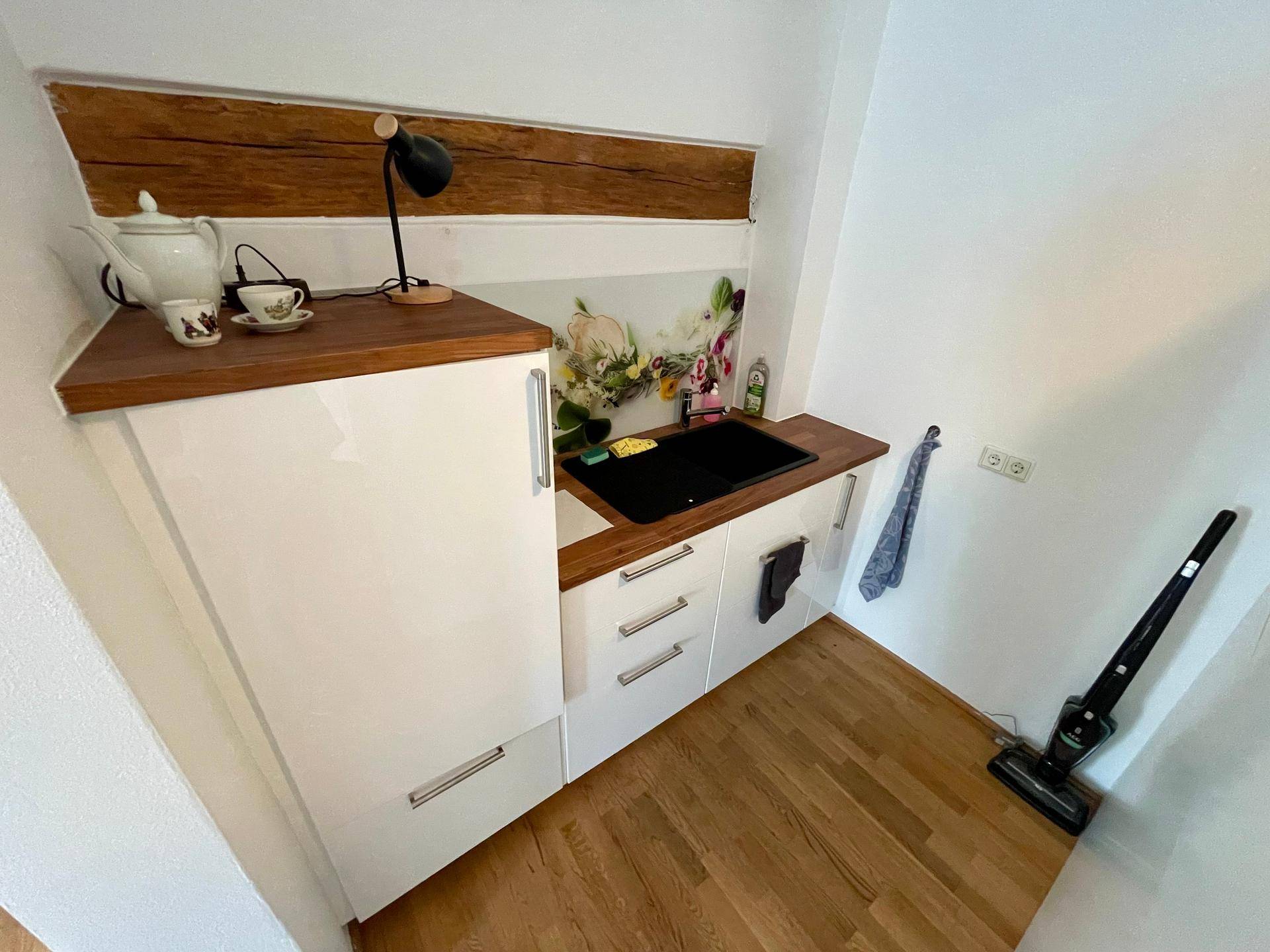 Kompakte Küchenzeile mit Holz-Arbeitsplatte, Spüle und weißen Schränken in einer Nische.