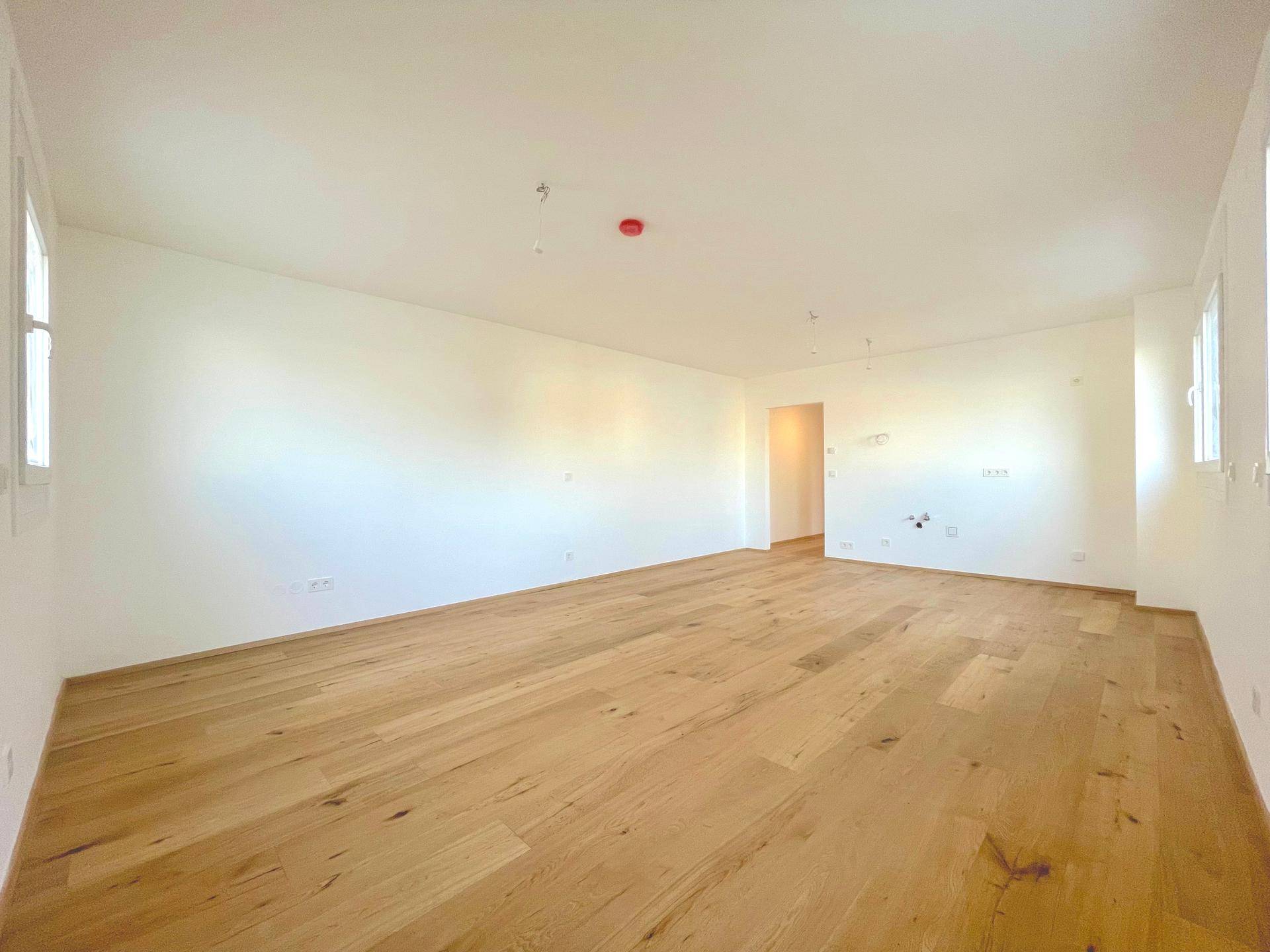 Heller Wohnbereich mit neuem Holzfußboden und weiß gestrichenen Wänden, bereit zum Einzug.