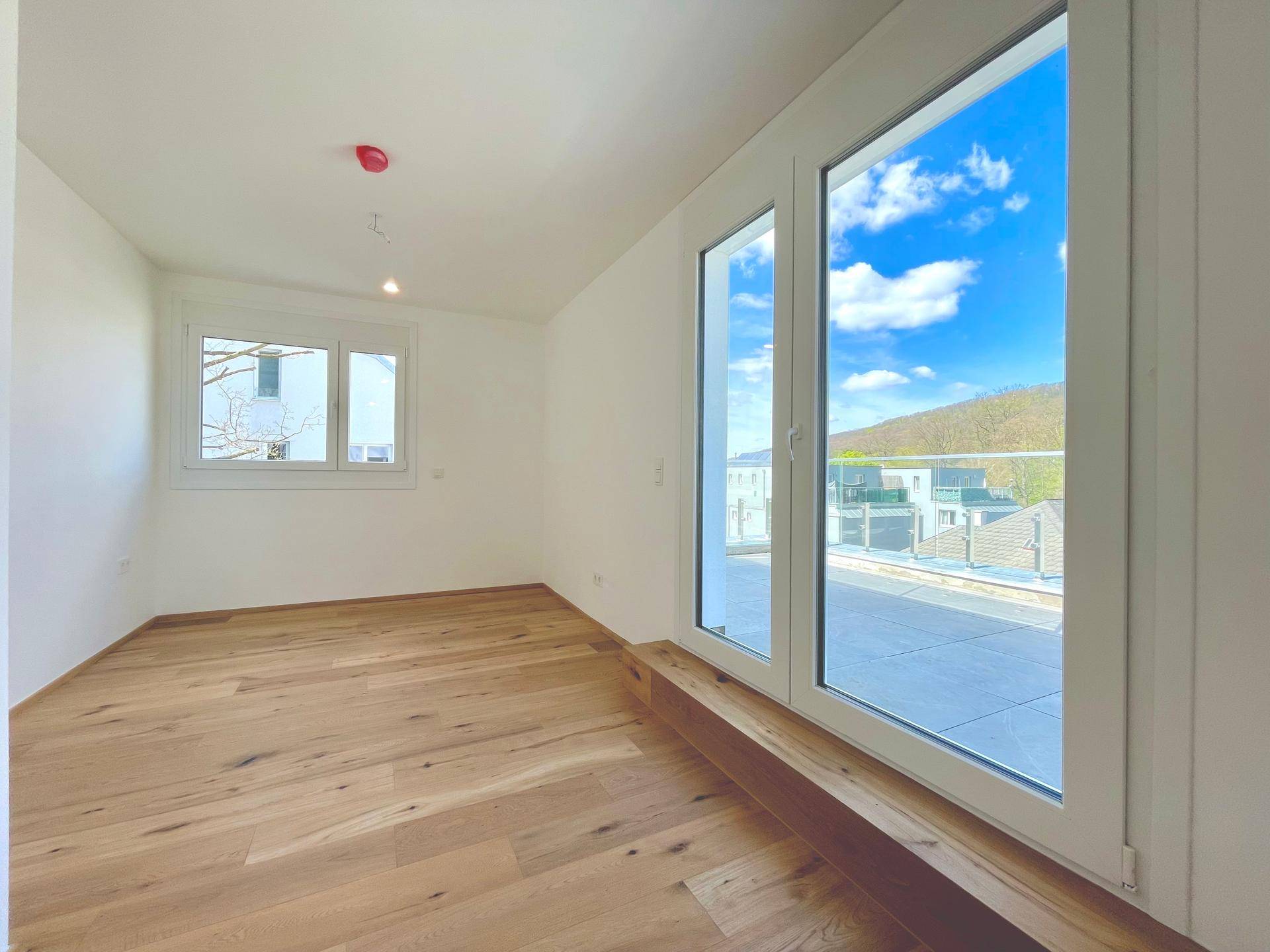 Helles Schlafzimmer mit Holzboden und Zugang zu einem Balkon, bietet viel Tageslicht.