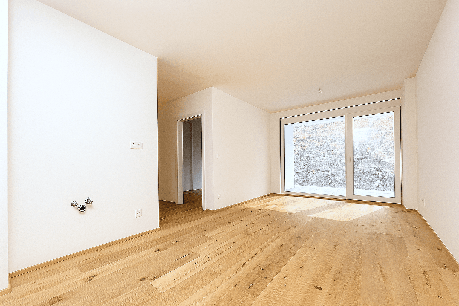 Heller, leerer Raum mit Holzboden und großer Fensterfront zum Außenbereich.